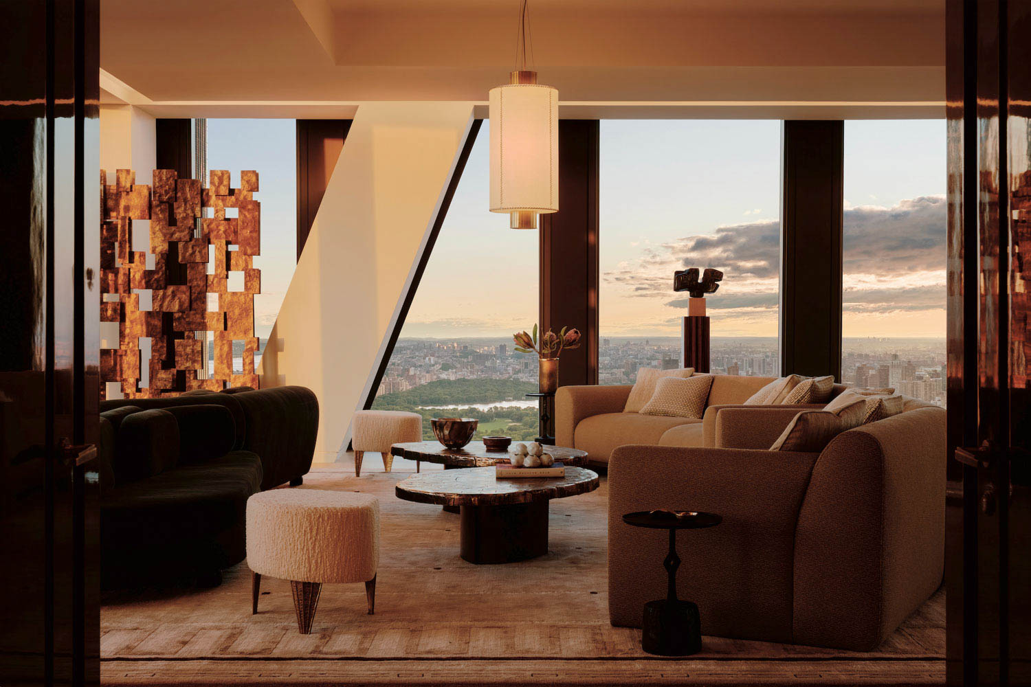 Modern living room with neutral furniture, abstract decor, large windows, and a cityscape view at sunset. Warm lighting highlights a minimalist yet cozy interior design.