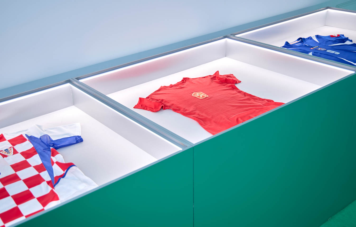 Three soccer jerseys are displayed in glass cases: a red one in the center, a blue one on the right, and a red-and-white checkered one on the left.