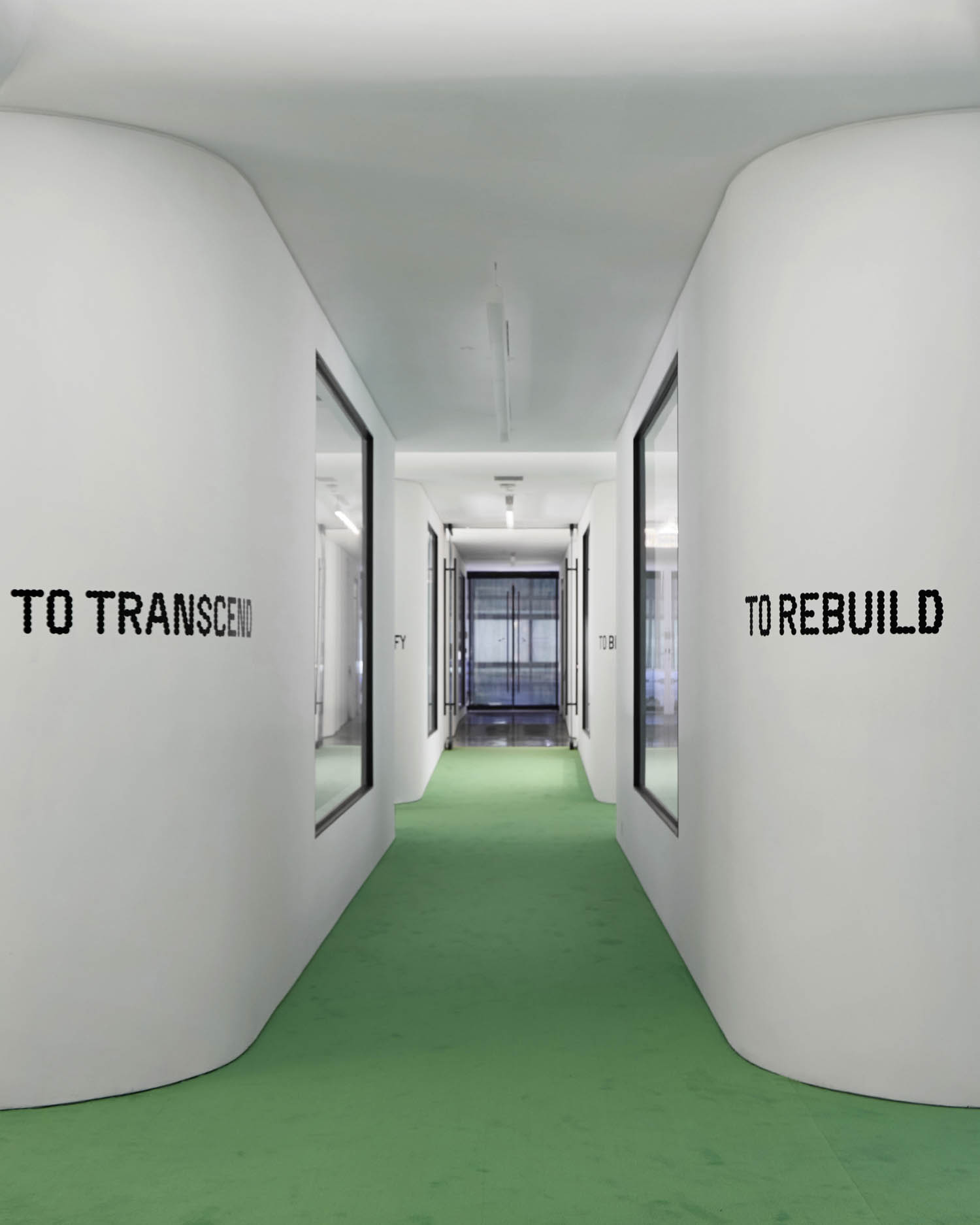 A hallway with white curved walls, green carpet, and large windows; the walls display the words "TO TRANSCEND" and "TO REBUILD" in black text.