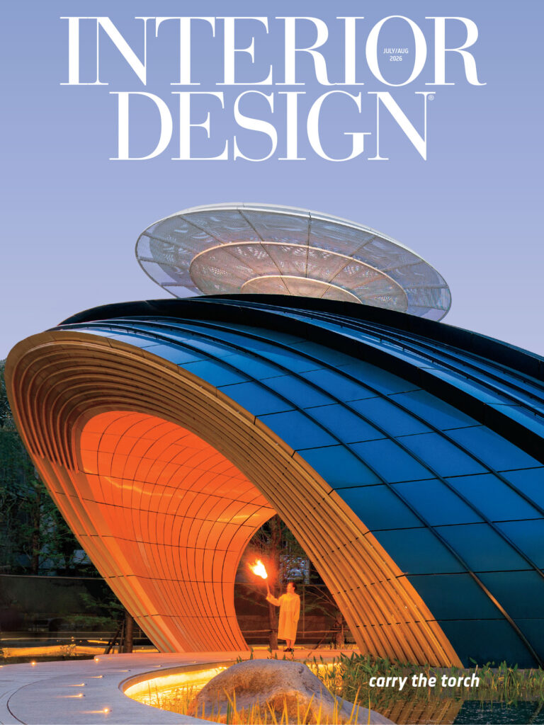 A modern, curved building with glowing orange interior lighting and a person holding a torch, featured on the cover of Interior Design magazine.