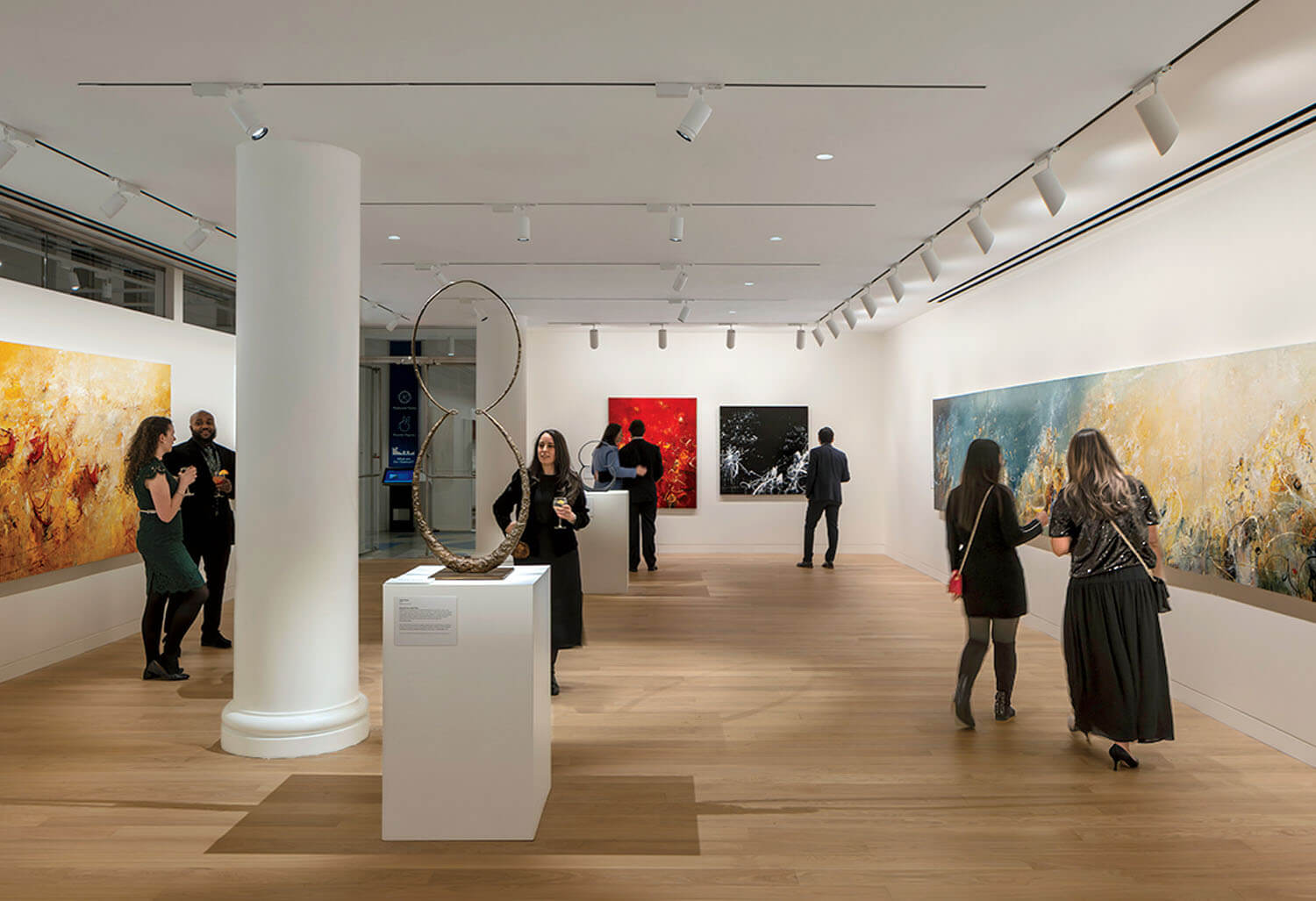 People view abstract paintings and a sculpture in a modern art gallery with white walls, wooden floors, and bright overhead lighting.