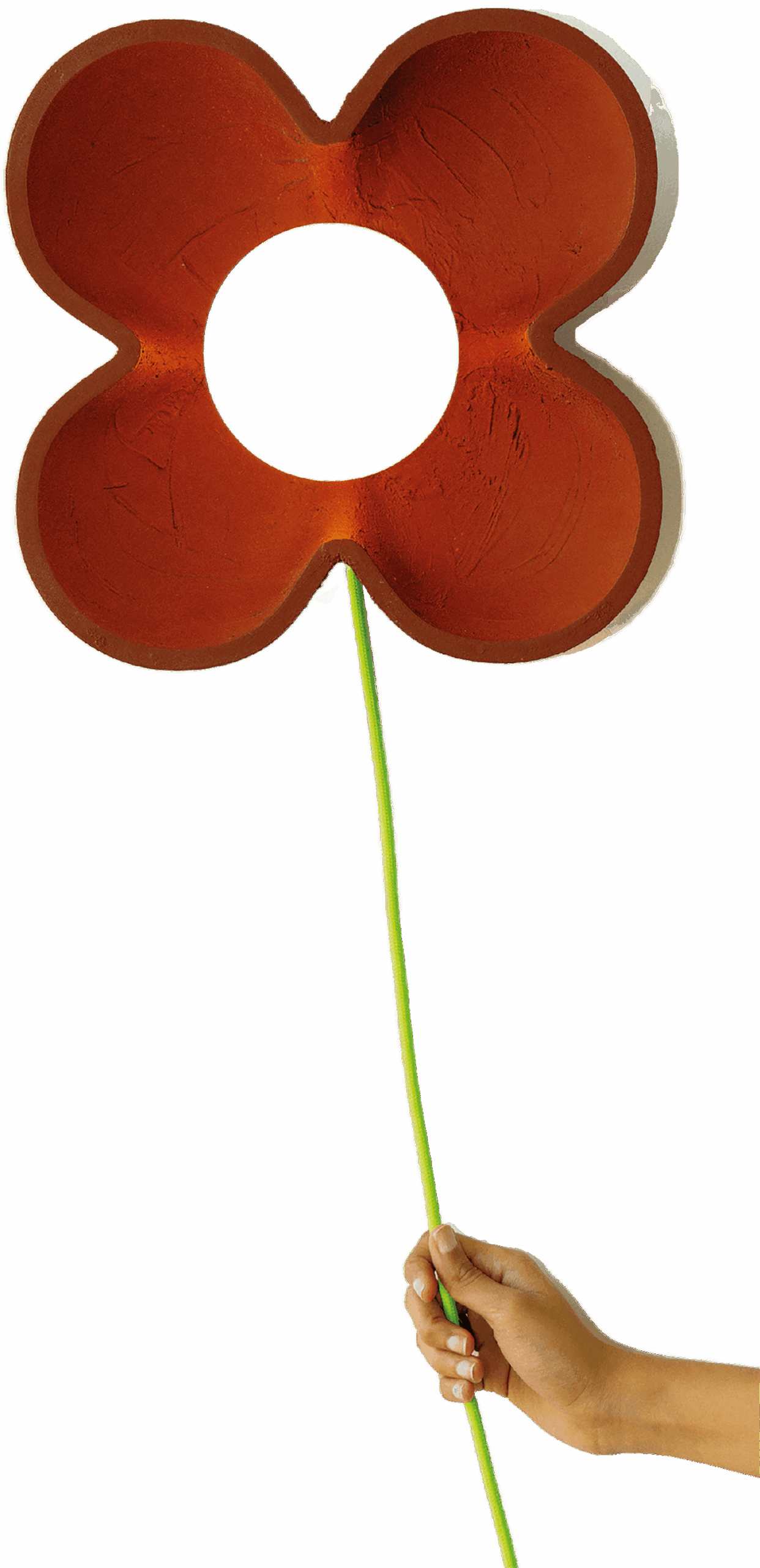 A hand holds a thin green stem attached to a flat, red, four-lobed flower shape with a large circular hole in the center, against a white background.