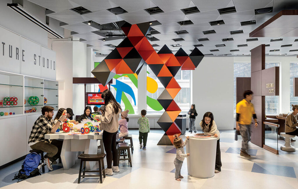 People of various ages engage in hands-on activities and crafts in a bright, modern space with geometric art installations and display shelves.