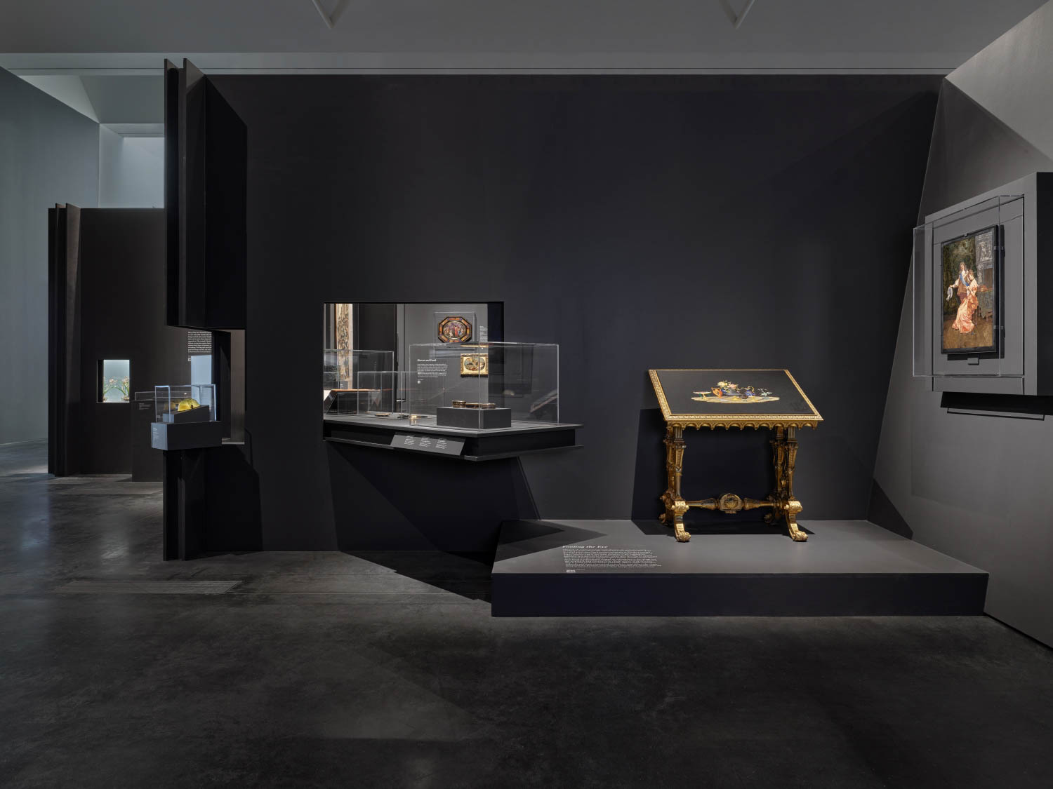 A museum gallery with dark walls displays artwork, artifacts in glass cases, a gold-trimmed table with items, and a framed portrait on the right wall.