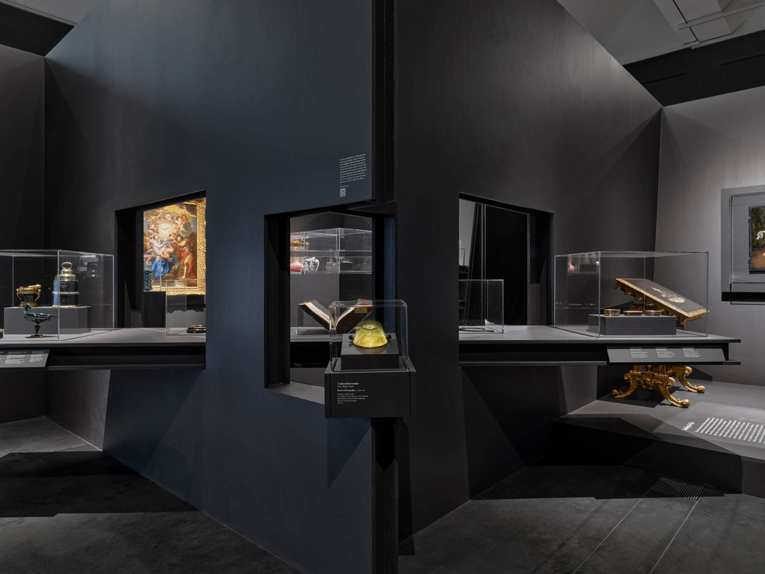 Museum exhibit displays various historical artifacts and books in glass cases within a modern, dark-walled gallery space.