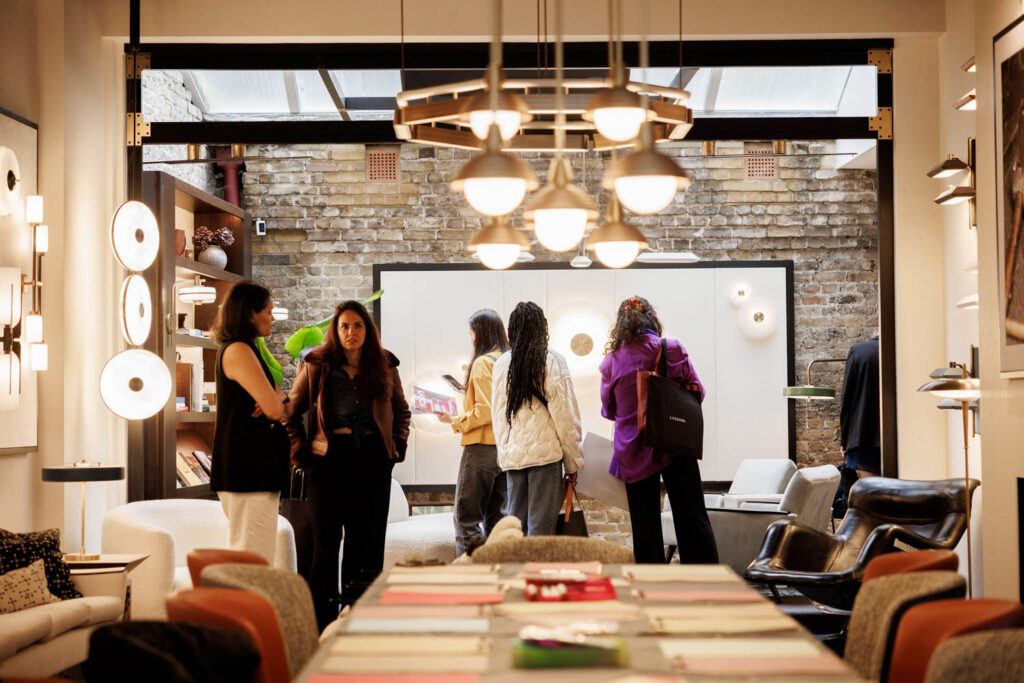 A group of people gather and converse inside a modern, well-lit showroom with contemporary furniture and lighting fixtures on display.