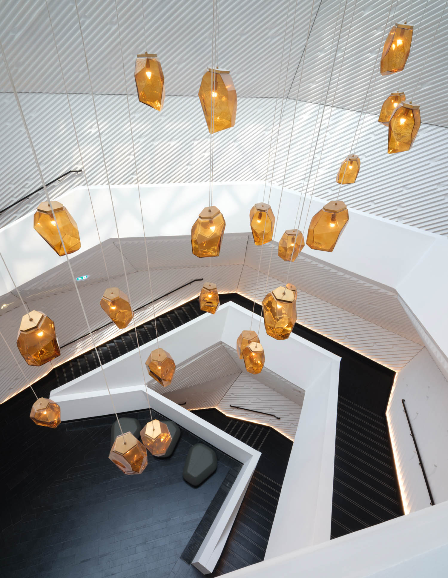 Cluster of geometric amber pendant lights hanging above a modern, white angular staircase with black steps, viewed from above.