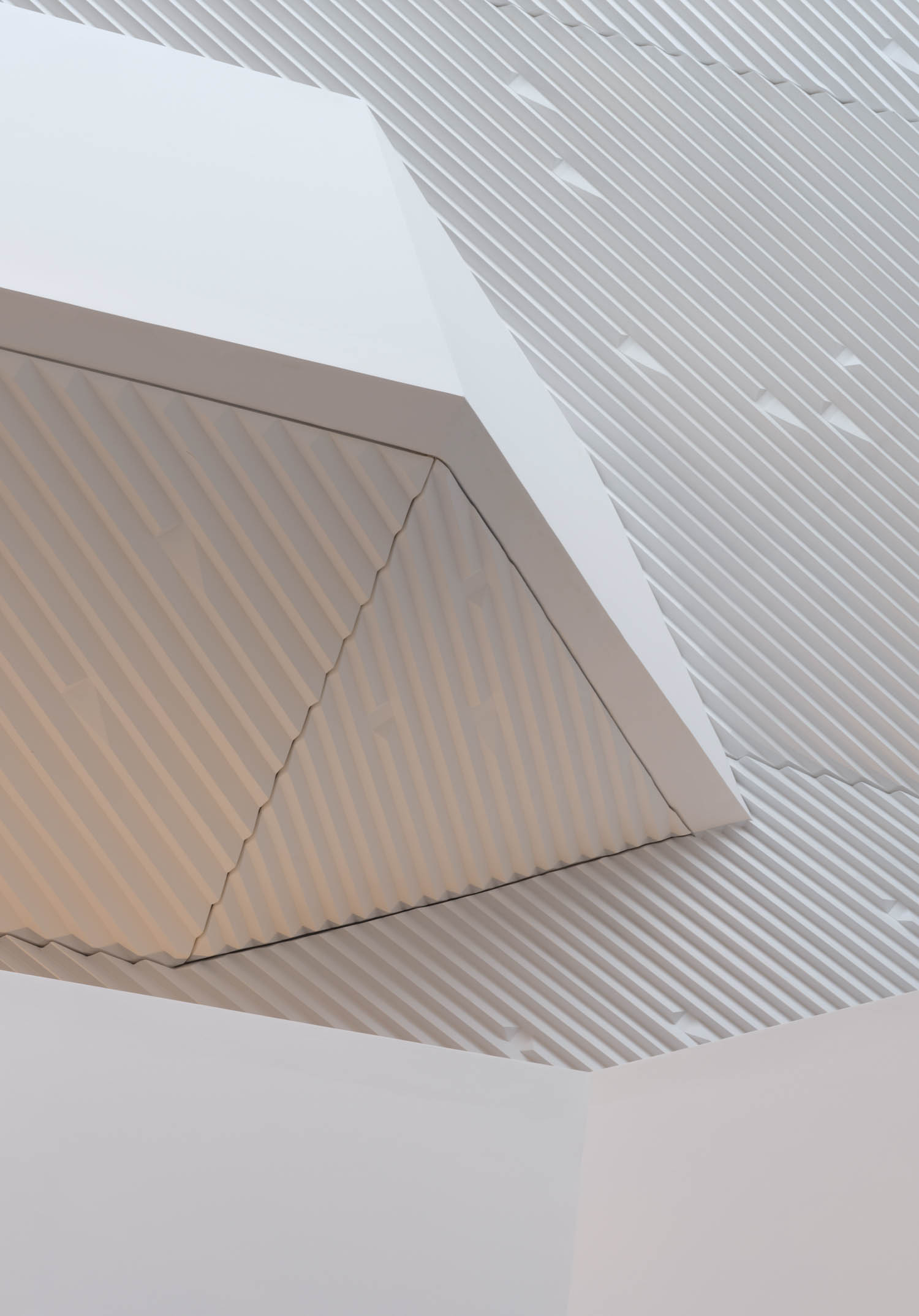 Geometric white ceiling with angular shapes and diagonal striped patterns in varied directions, creating a modern architectural design.