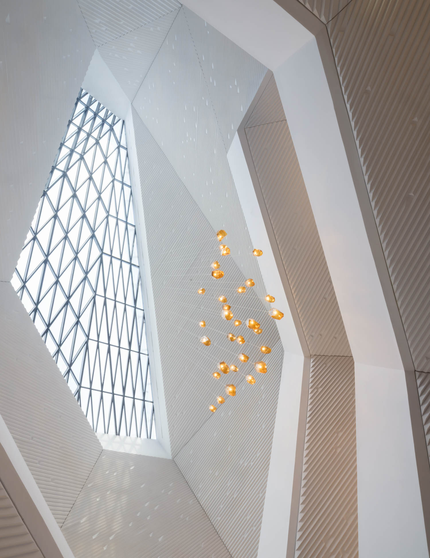 Geometric skylight ceiling with a grid window and modern hanging lights, viewed from below in a minimalist architectural space.