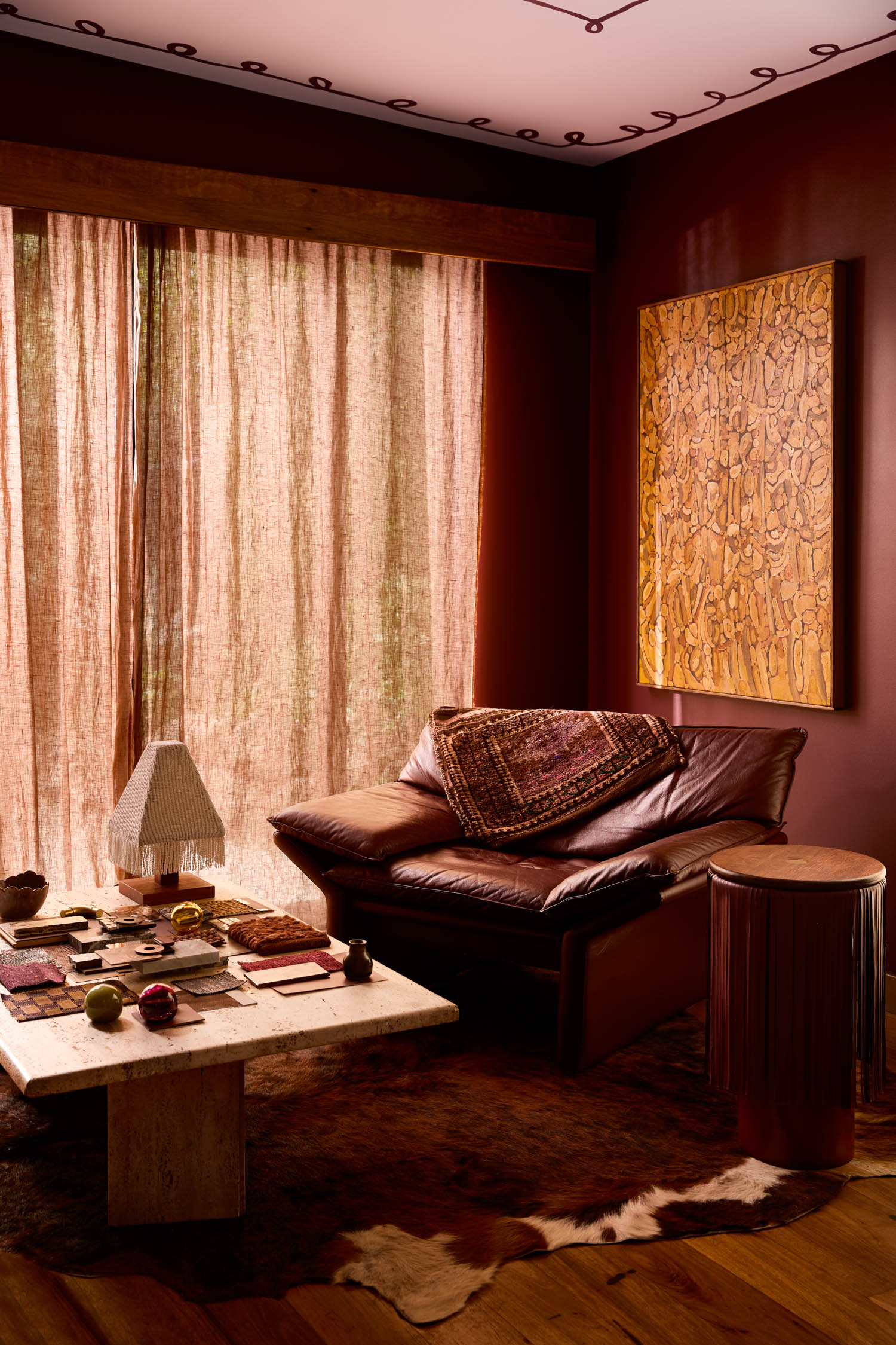 Cozy living room with brown leather sofa, abstract wall art, coffee table with decor, floor lamp, and sheer curtains letting in natural light.