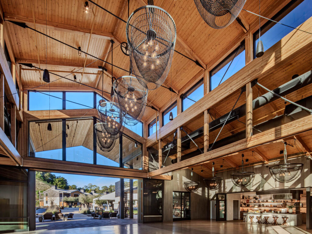 Spacious modern lobby with high wooden ceilings, large windows, hanging woven light fixtures, and a small bar area on the right.