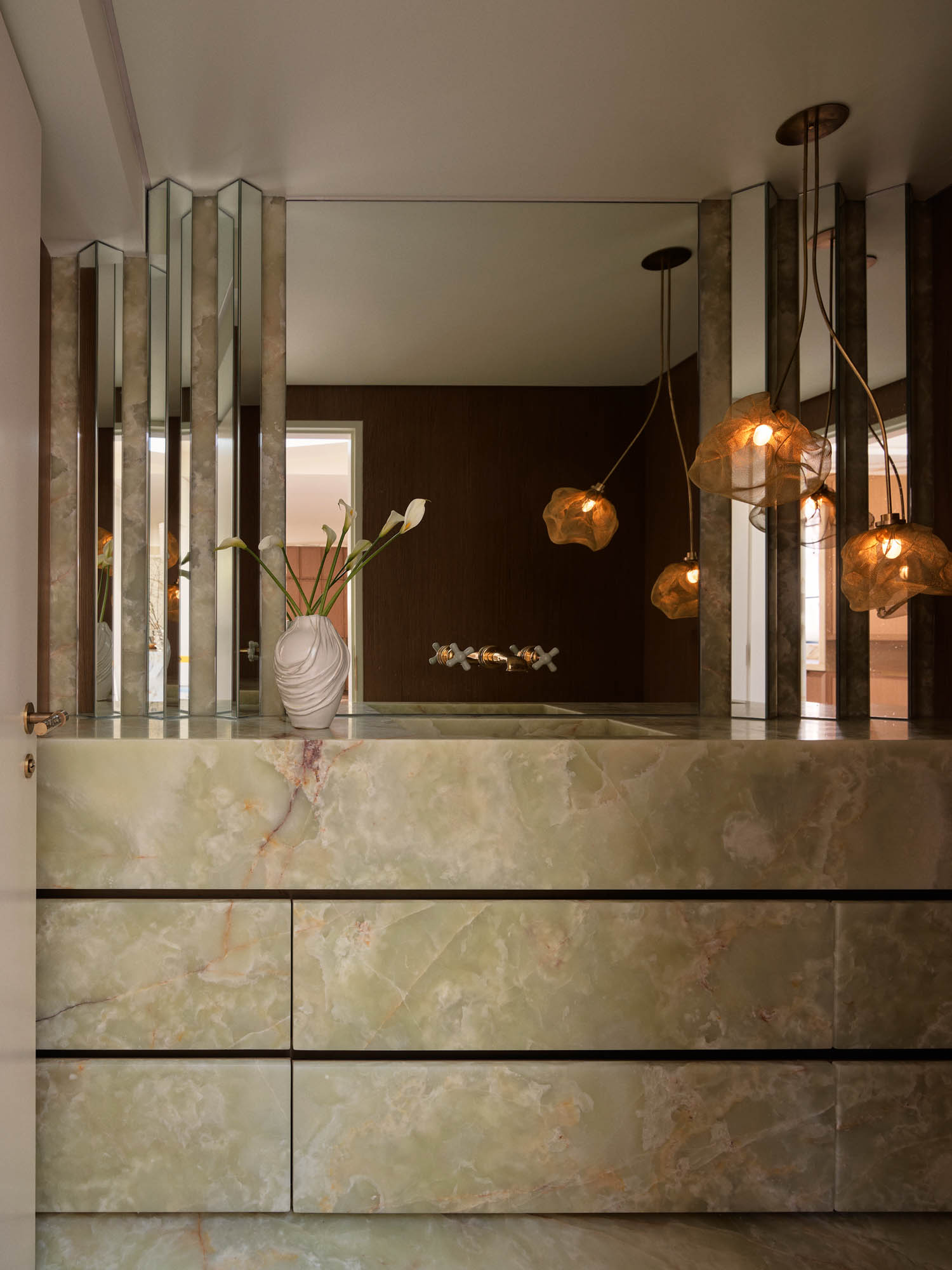 Modern bathroom with green marble vanity, a large mirror, vertical mirrored panels, pendant lights, and a white vase with flowers on the counter.