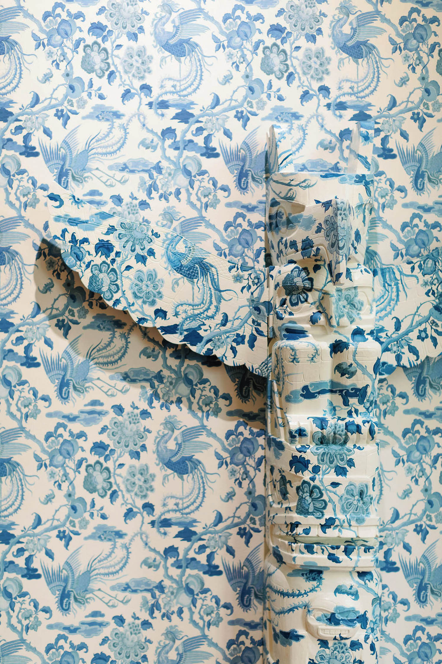 A person in clothing matching the blue and white floral wallpaper stands against the wall, blending in with the pattern.