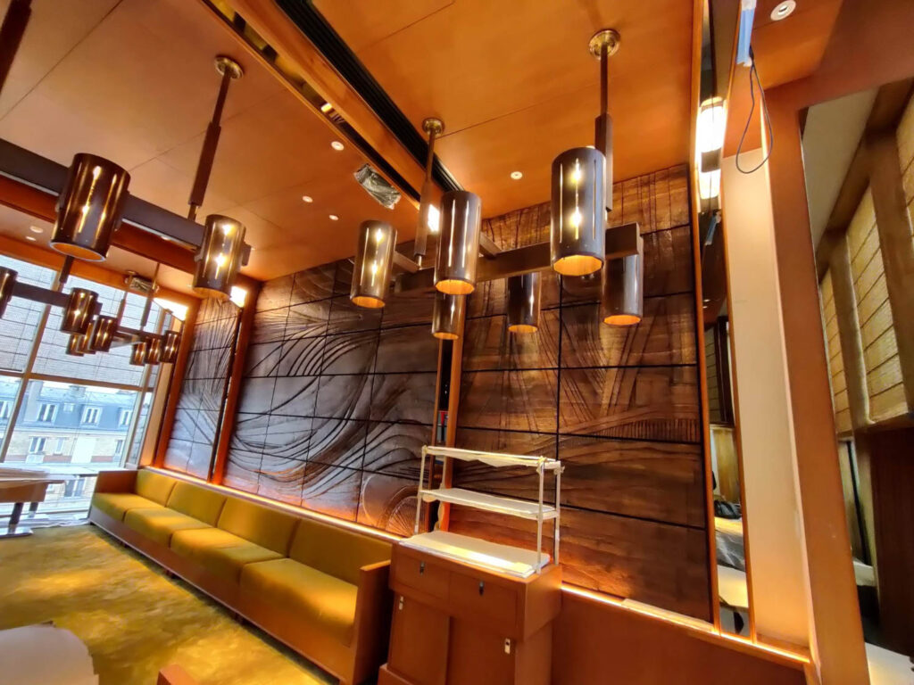 Modern interior room with wooden panel walls, ceiling lights, a long yellow-green sofa, large windows, and metal shelving by the wood-paneled feature wall.