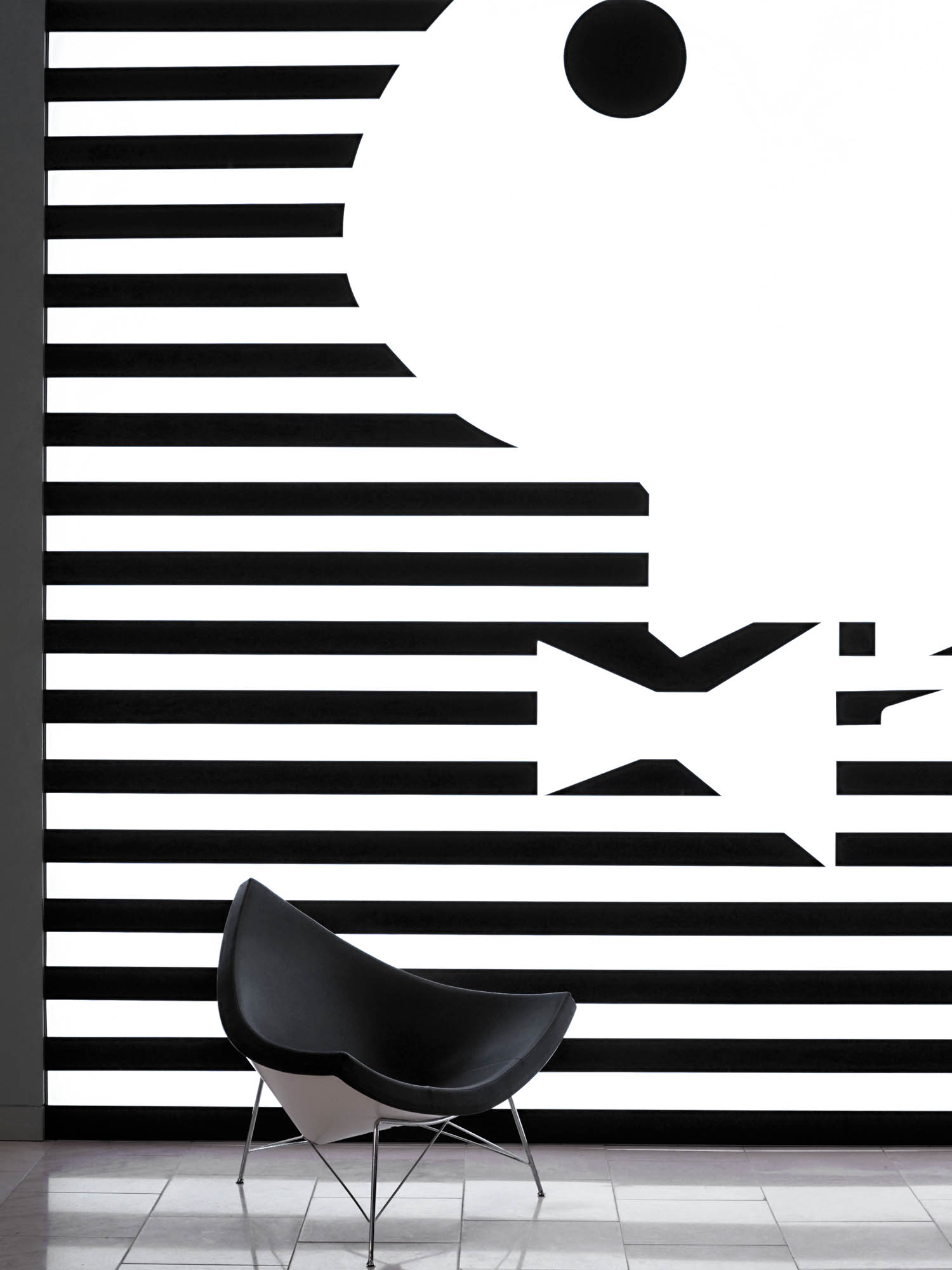 Black modern chair in front of a wall with bold black and white horizontal stripes and abstract geometric shapes.