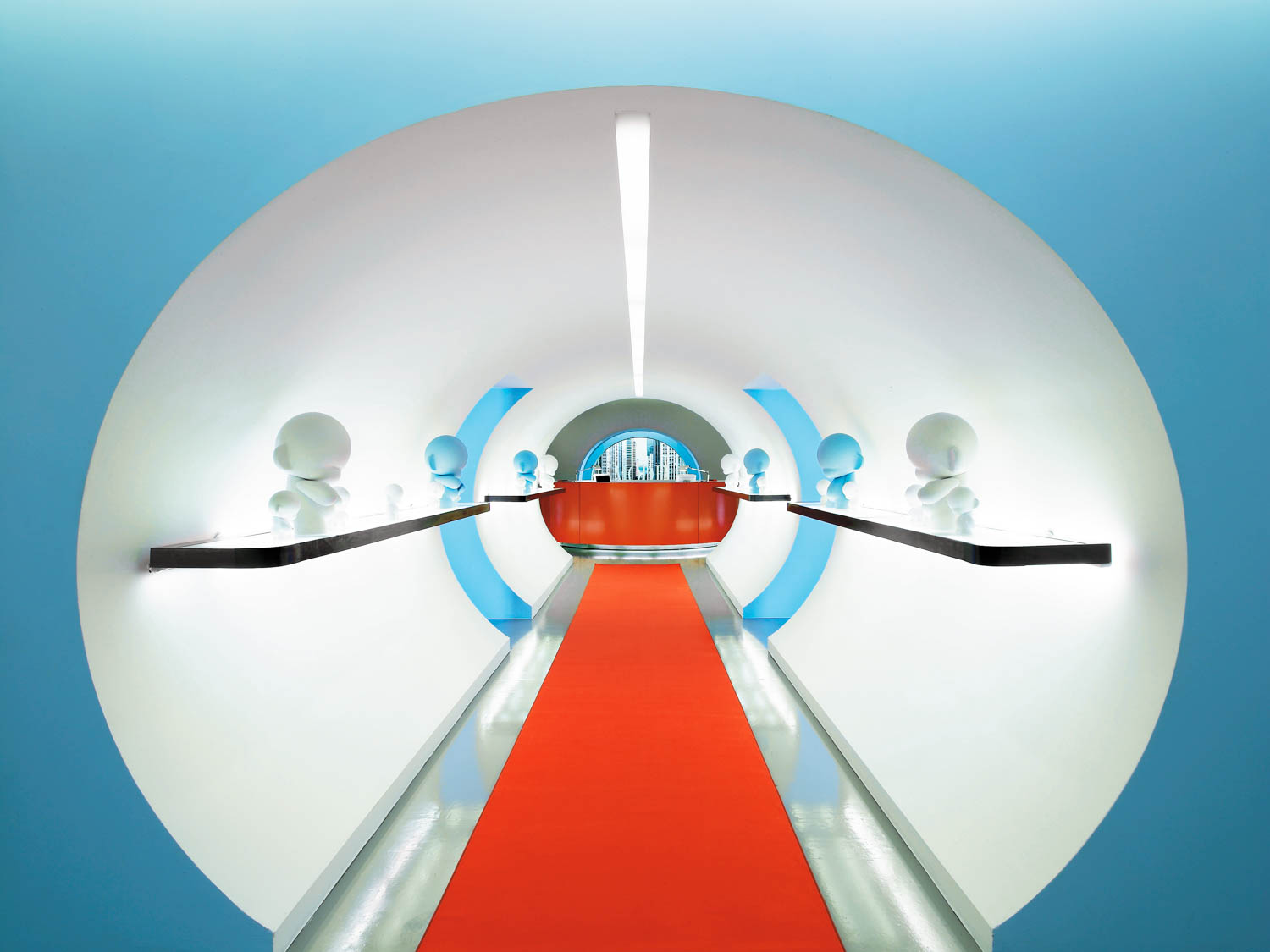 A futuristic hallway with a red carpet, white walls, blue accents, and small white figurines displayed on black shelves along both sides.