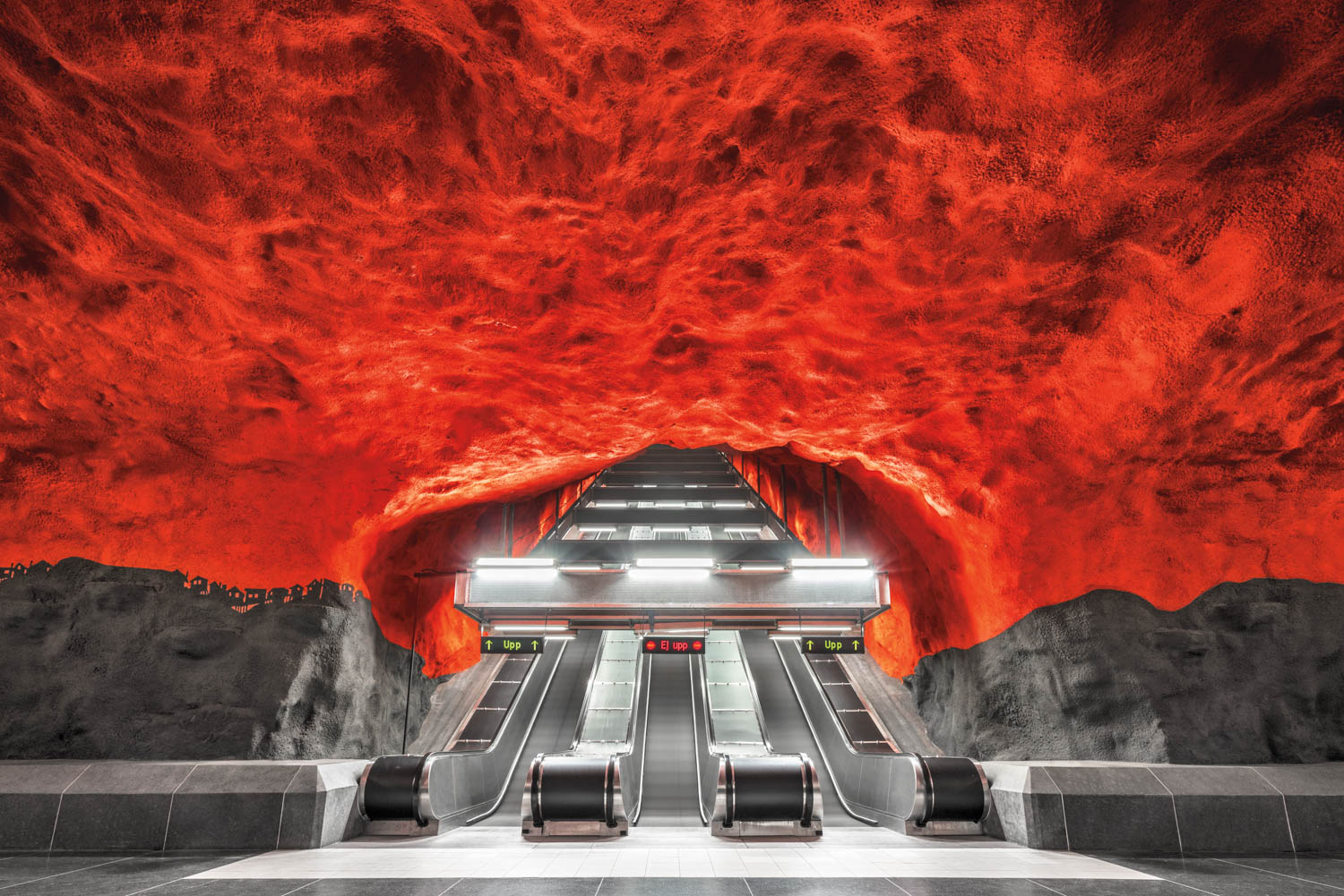 Three escalators lead up from a subway station with a dramatic red, cave-like ceiling and dark rocky walls.