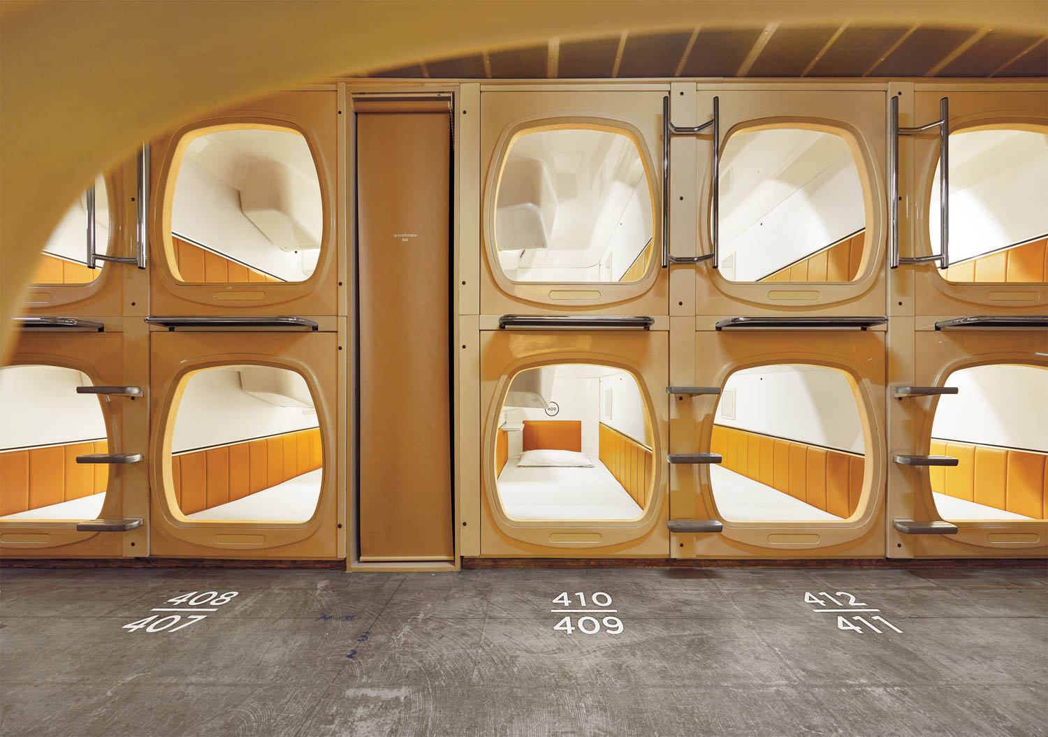 A row of stacked, individual capsule beds with numbered doors in a modern, minimalistic capsule hotel.