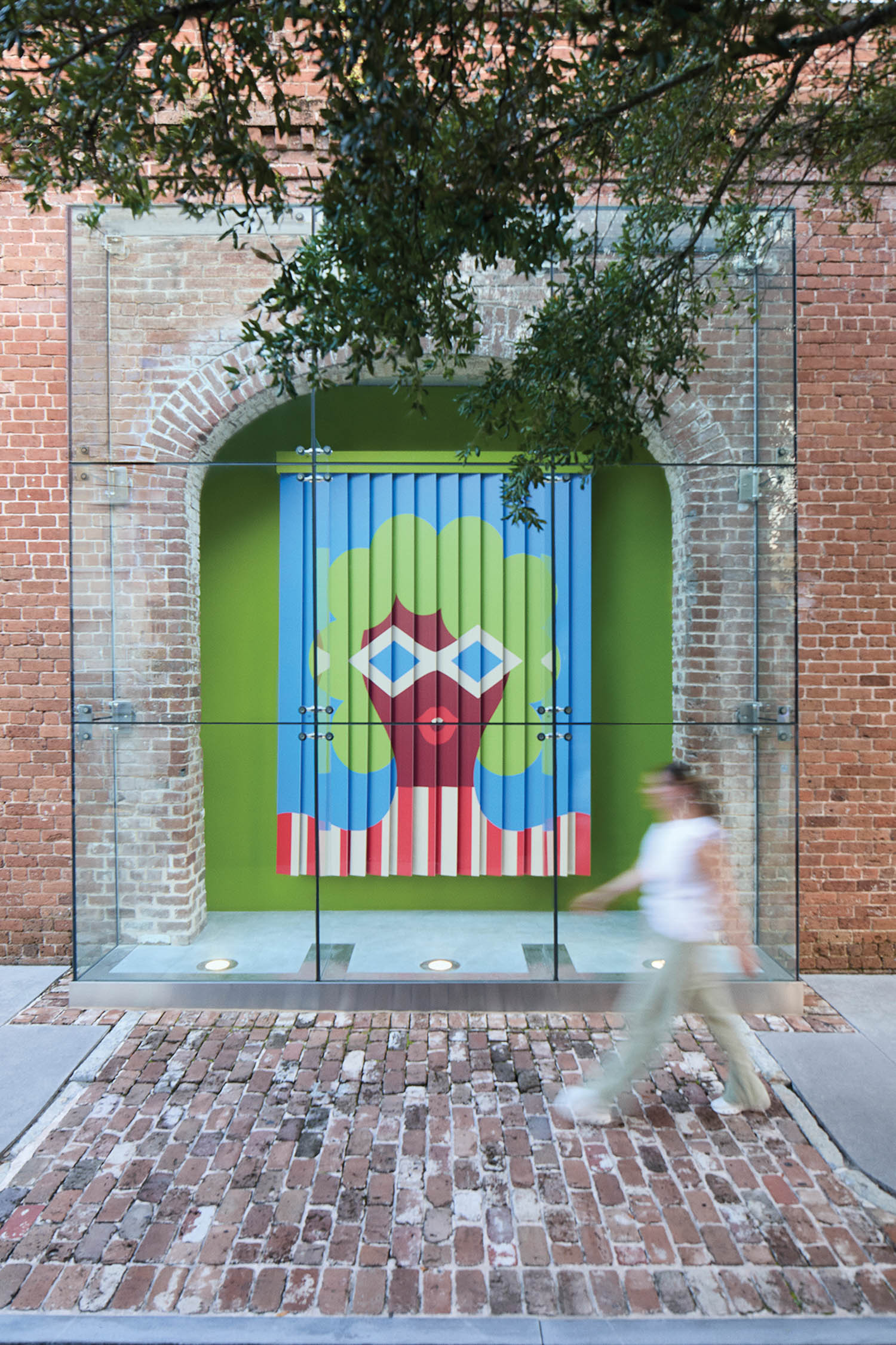 A person walks past a glass display featuring a colorful mural of a face with geometric shapes on a brick wall.