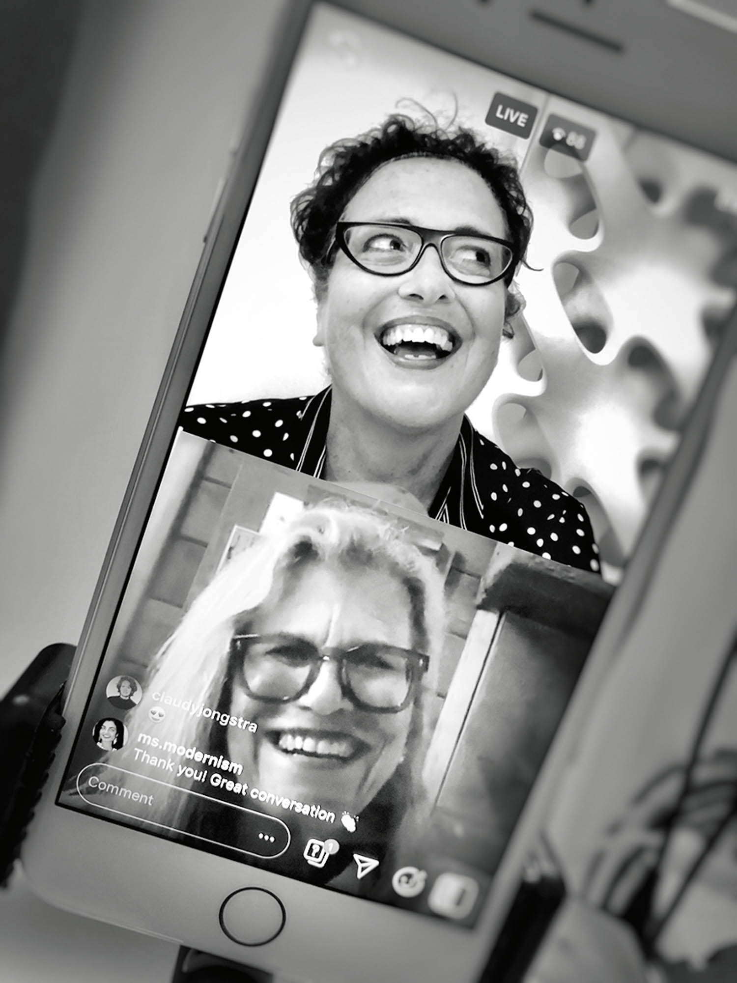 Two people smile and talk during a live video chat on a smartphone screen, shown in black and white.