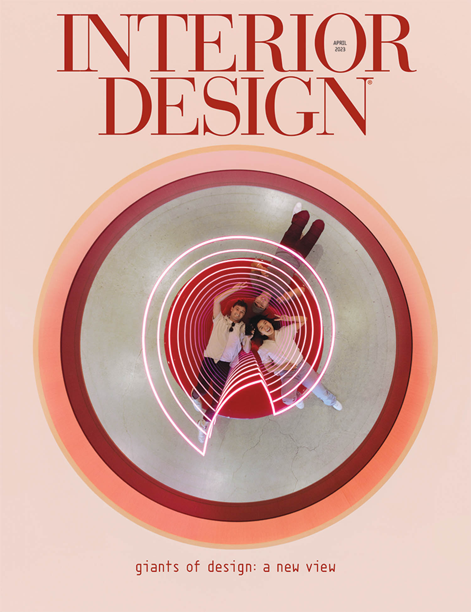Three people lie on a circular red seating area under a spiral neon light, viewed from above, on the April 2023 cover of Interior Design magazine.