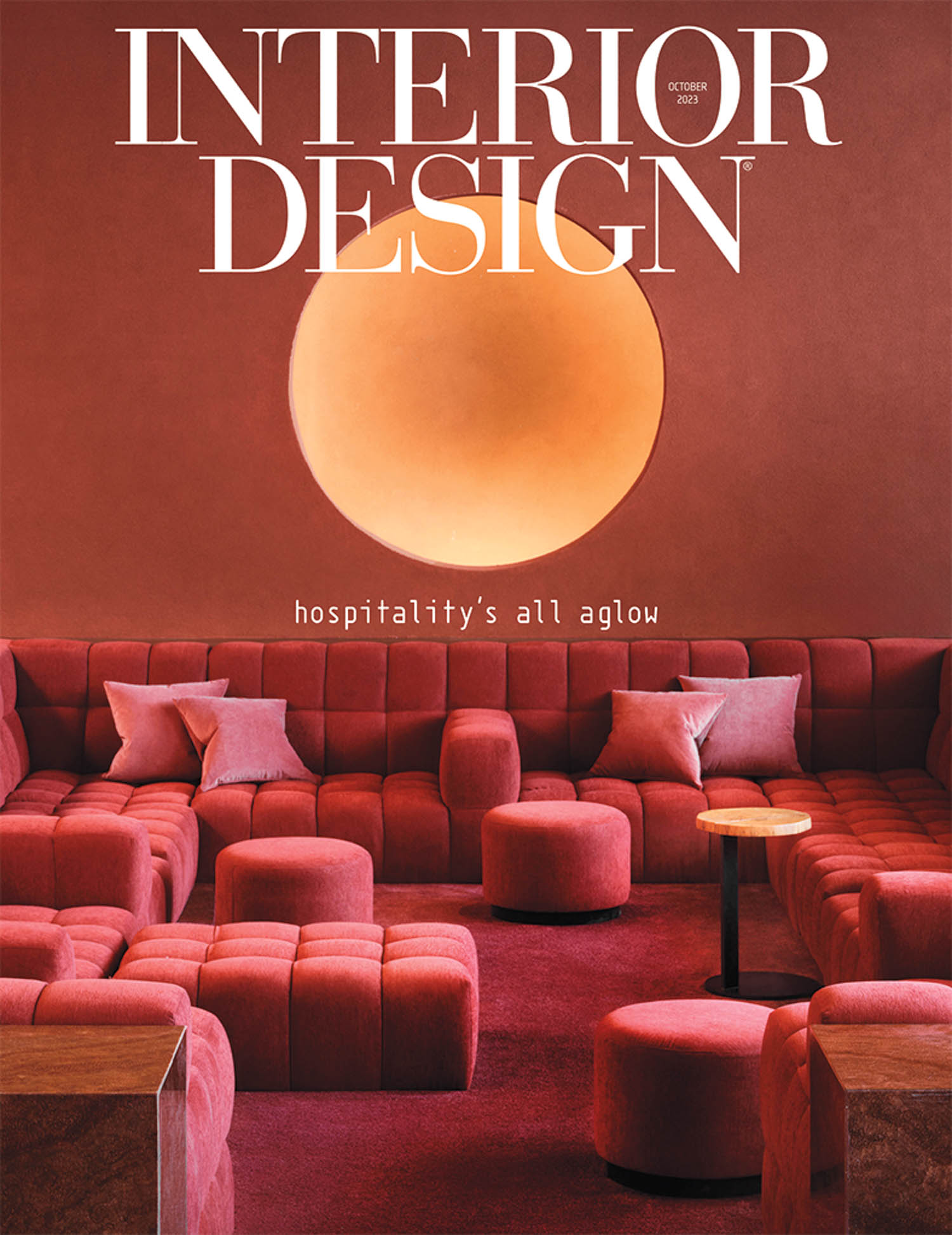 Interior Design magazine cover featuring a red-toned lounge with plush seating, round tables, and a large circular light on the wall. Text reads, “hospitality’s all aglow.”.