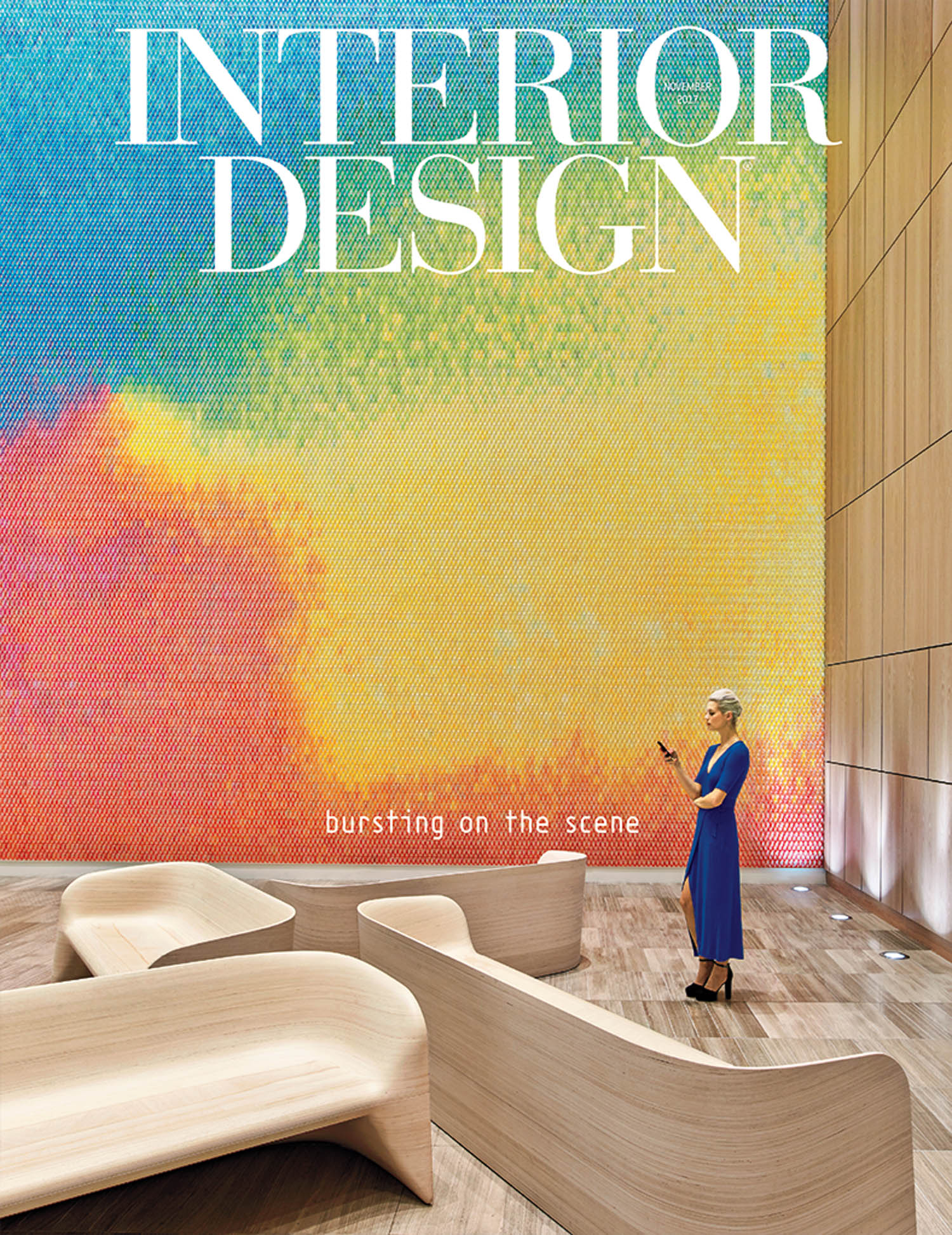 A woman in a blue dress stands near modern wooden benches in front of a large, colorful mosaic wall under the text “INTERIOR DESIGN.”.