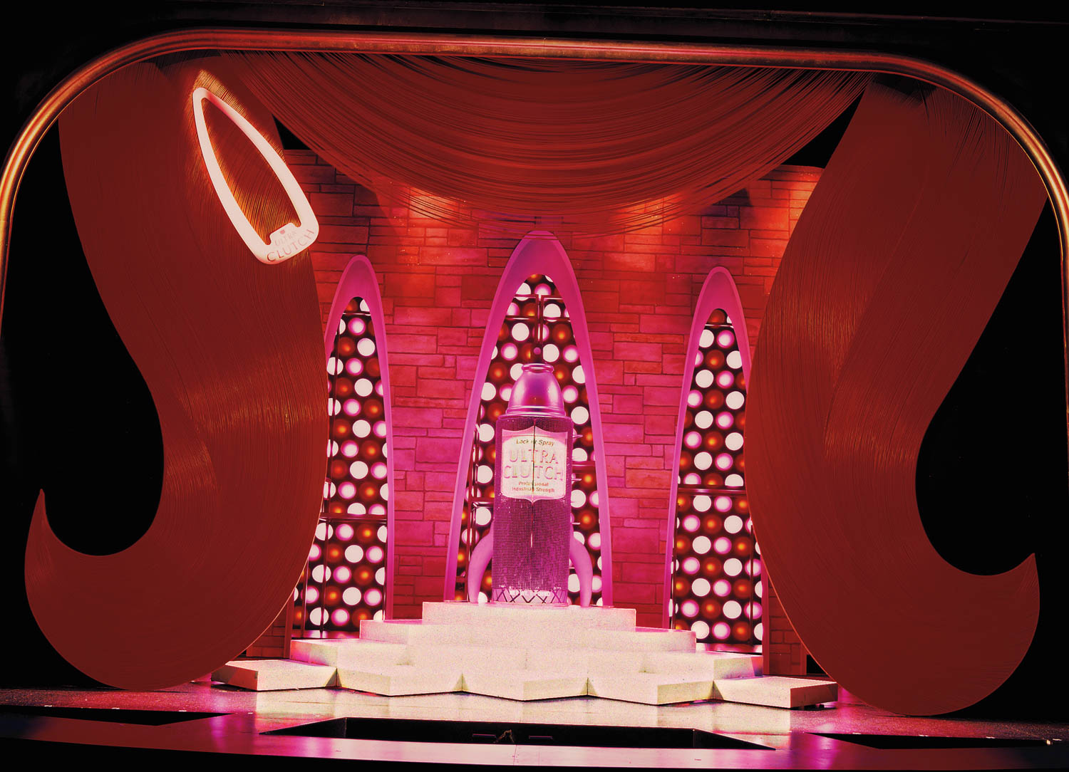 A brightly lit stage with large red curtain accents, illuminated stairs, and a podium reading “She Done Already Done Had Herses” at center stage.