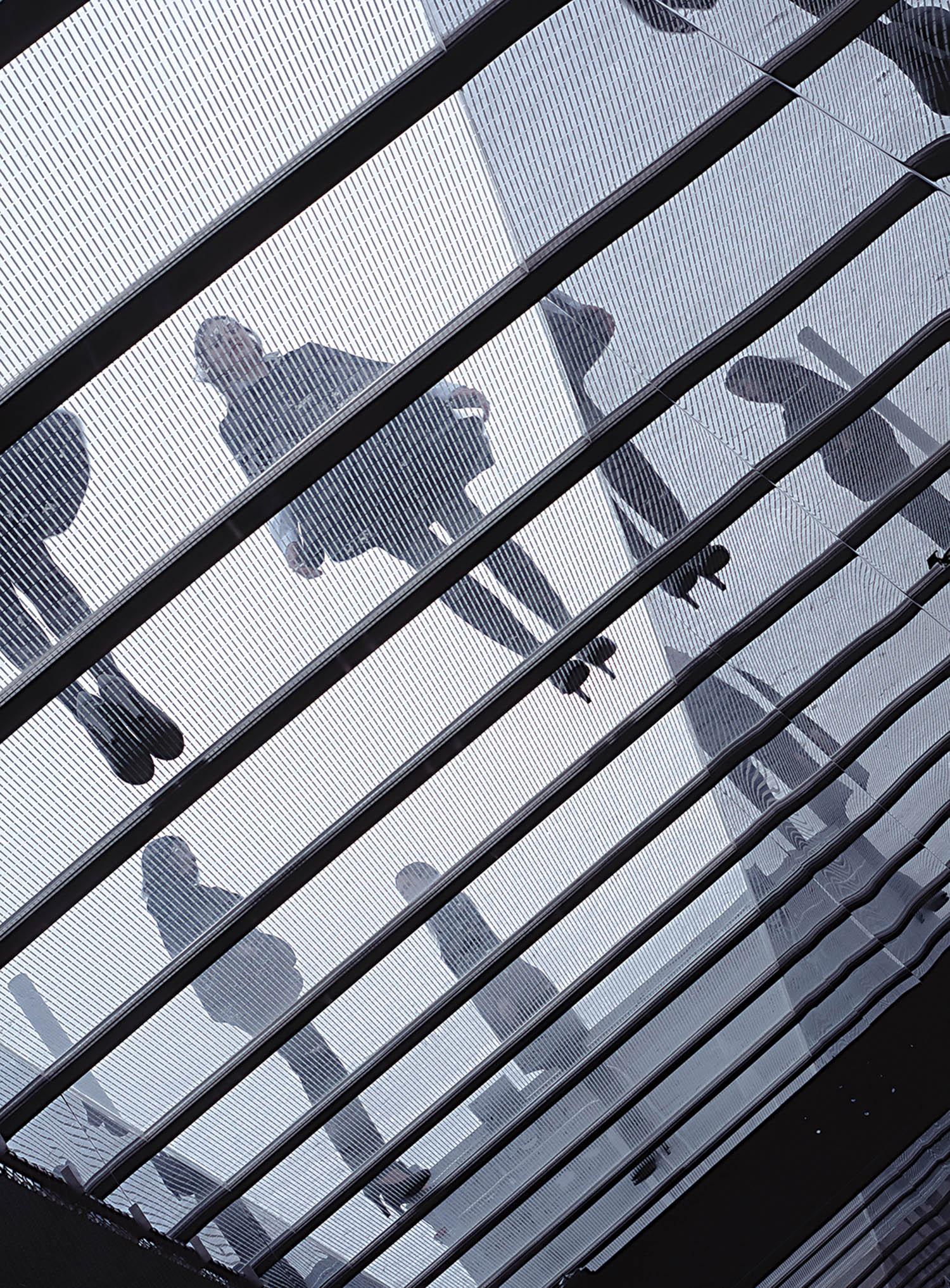 People walking on a transparent floor seen from below, with striped grid lines and silhouettes visible against a bright background.