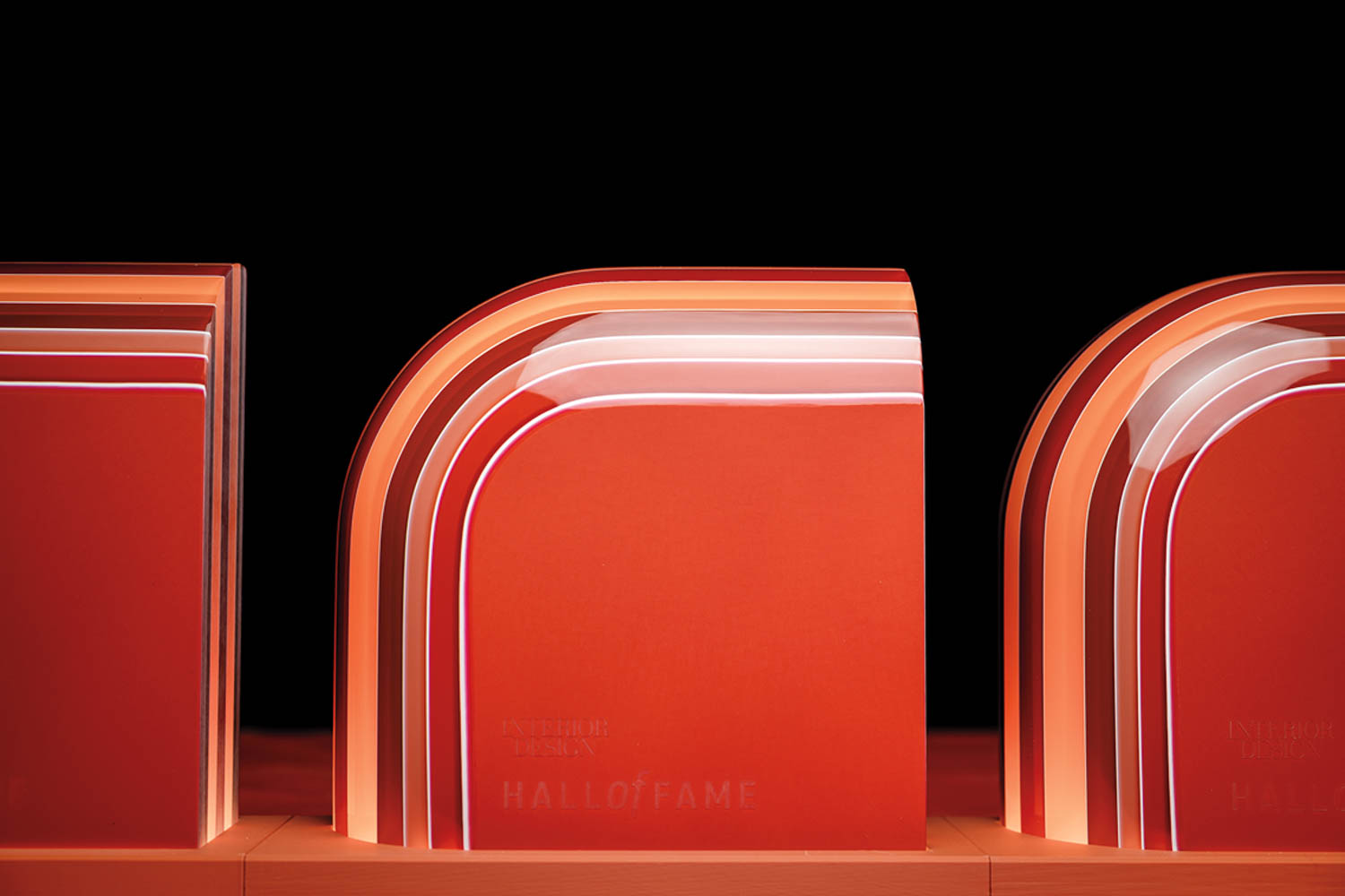 A red and clear curved glass award labeled “Interior Design Hall of Fame” sits on a wooden surface against a black background.