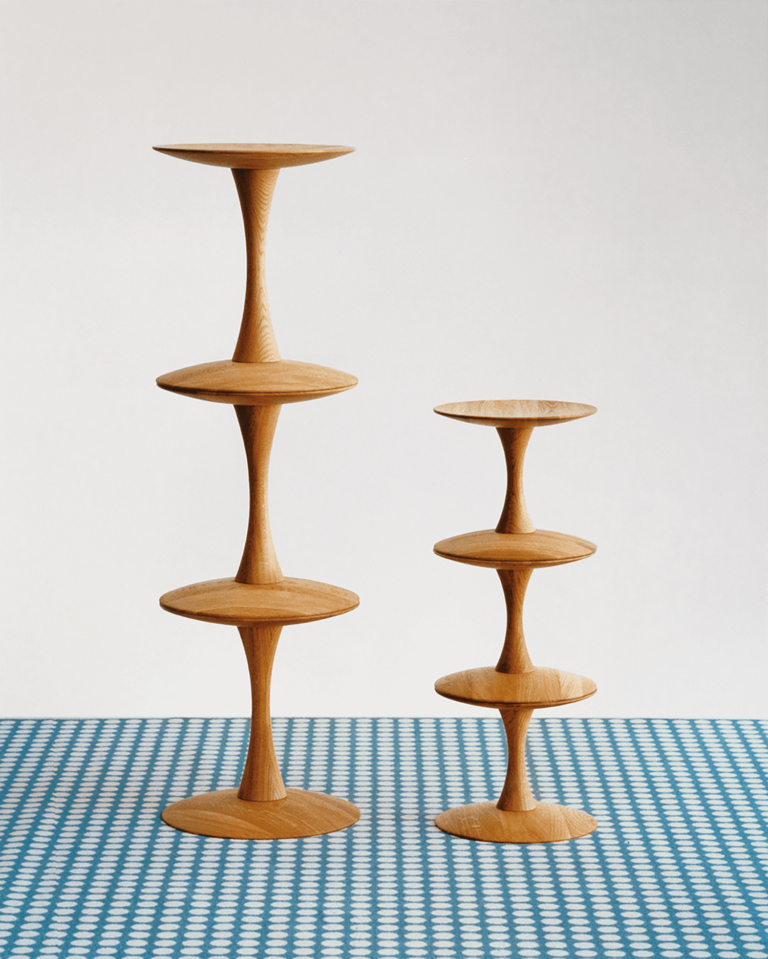 Two wooden, tiered pedestal stands of different heights on a blue and white patterned surface, against a plain background.
