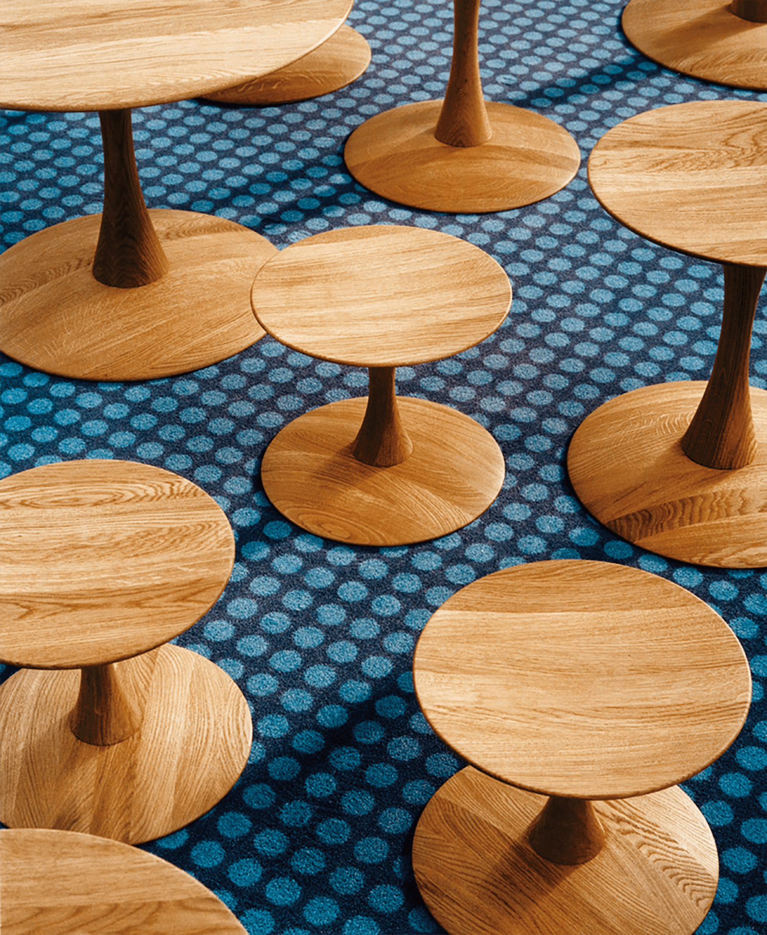 Several round wooden tables of varying heights are arranged on a blue carpet with a circular pattern.
