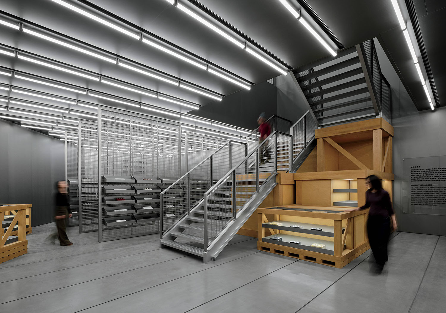 A modern, industrial-style interior with metal stairs, mesh shelves, concrete floors, and several people walking or standing.
