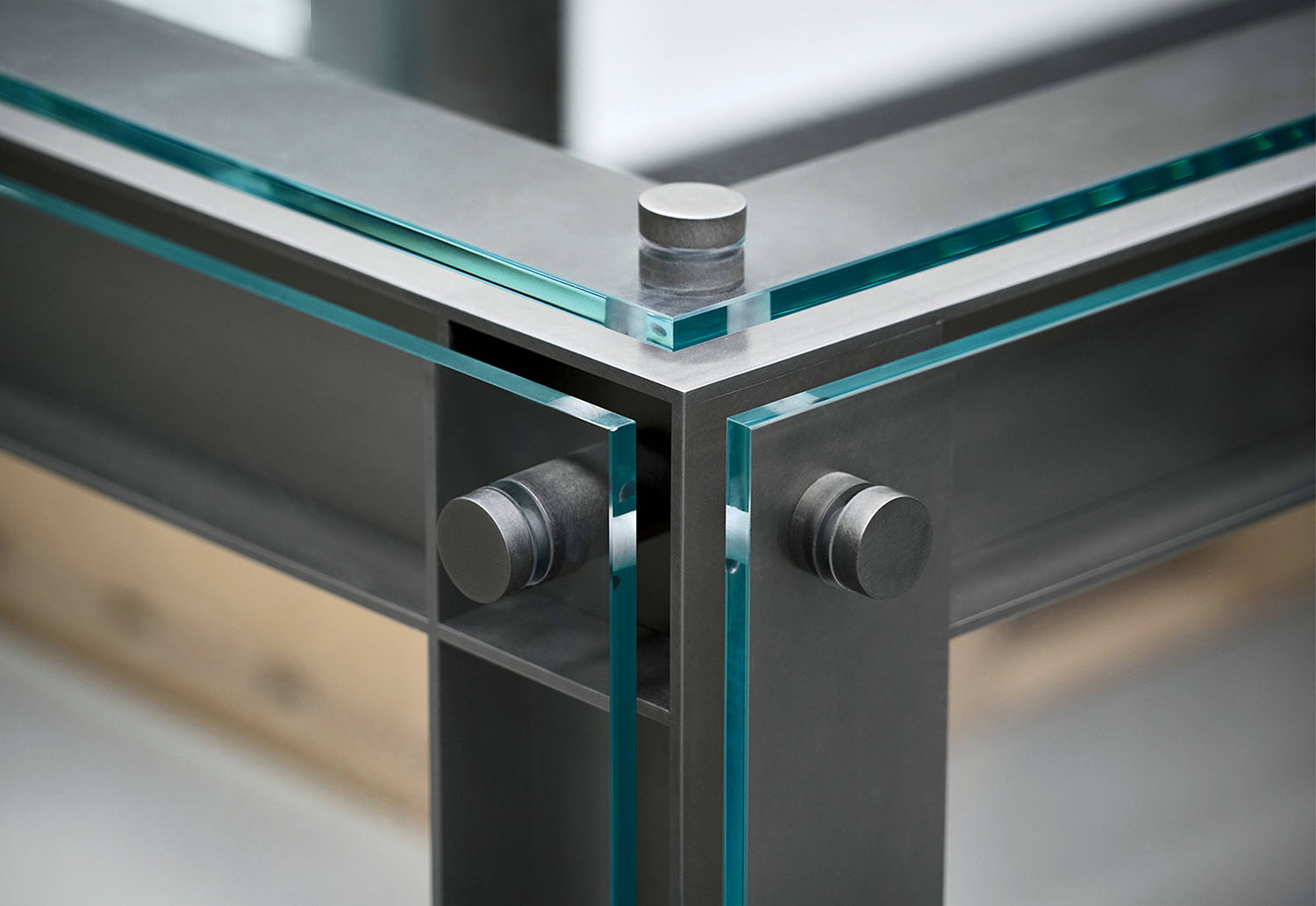 Close-up of a glass and metal corner joint with cylindrical fasteners securing transparent glass panels to a metal frame.