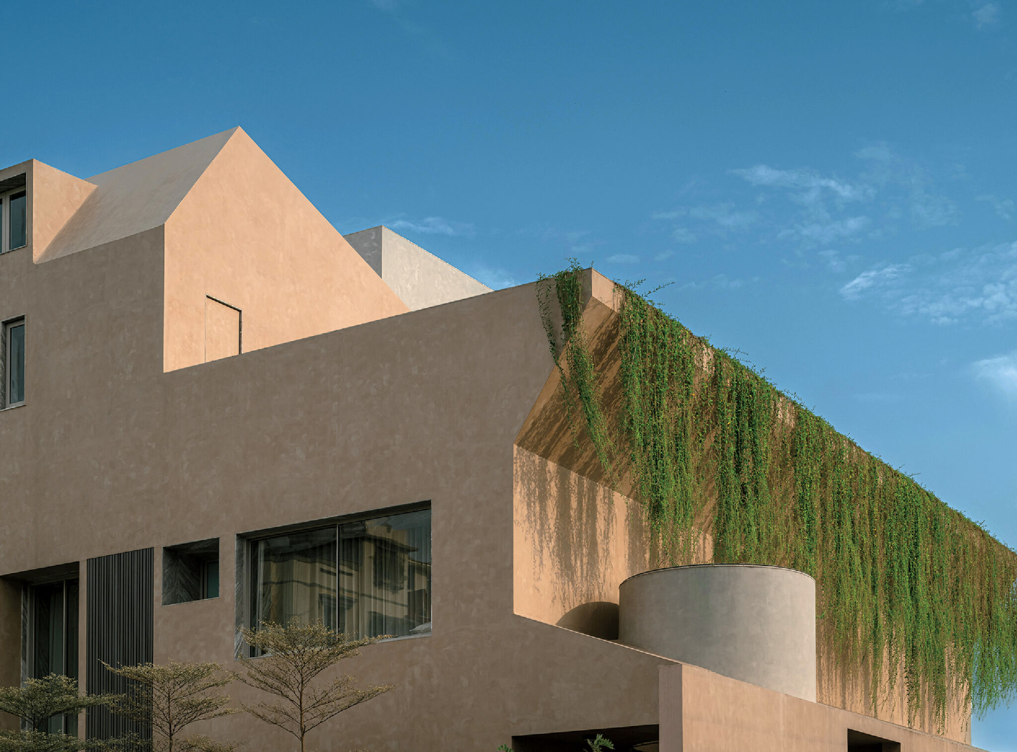 Modern beige building with large windows and cascading greenery on the facade, set against a clear blue sky.