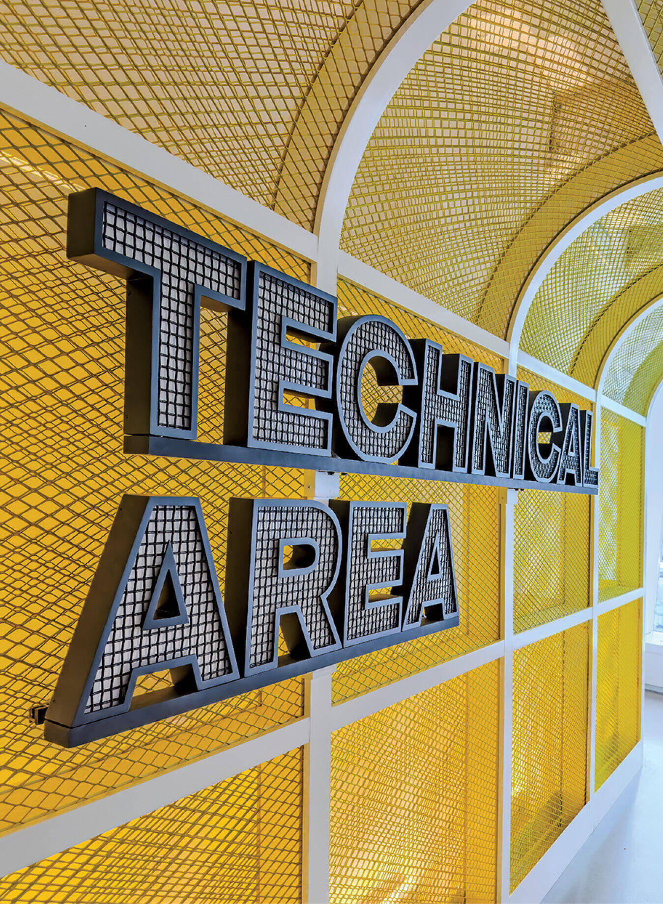 Large sign reading “TECHNICAL AREA” is mounted on a yellow, mesh-covered wall in a brightly lit interior space.
