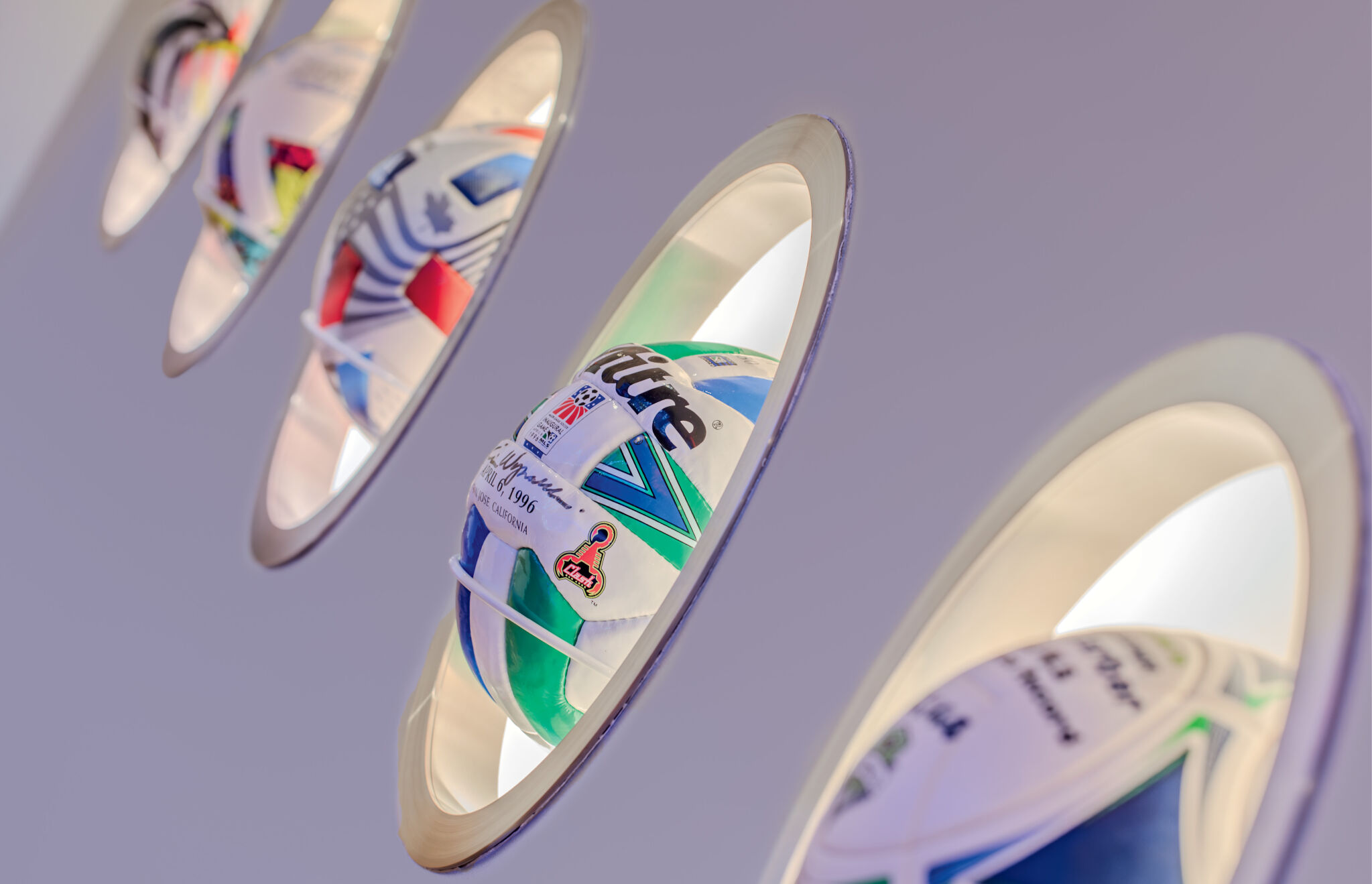 Close-up of rugby balls displayed in circular wall mounts, each partially lit from behind, with a focus on the ball in the foreground.