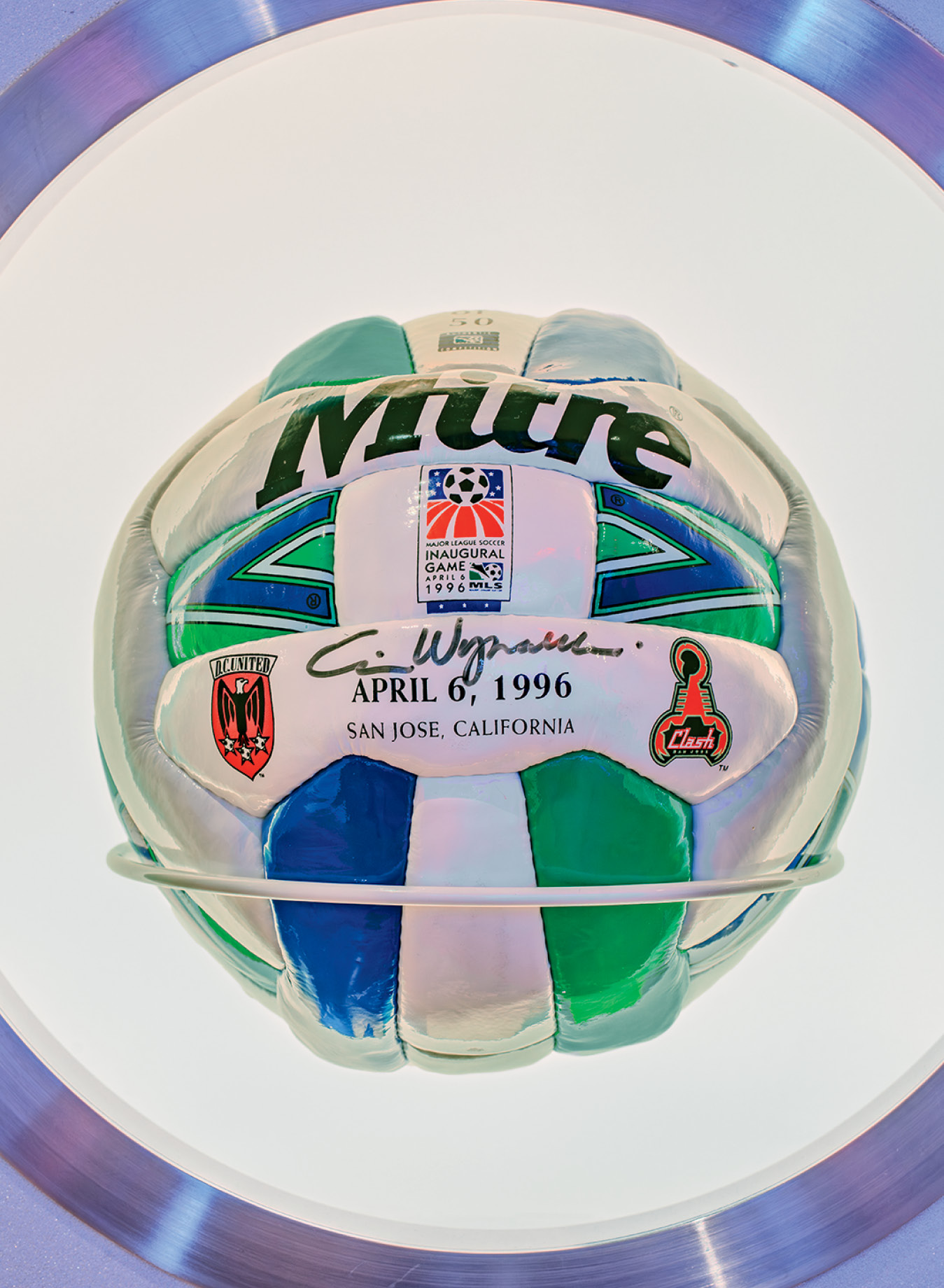A signed soccer ball commemorating the inaugural MLS game on April 6, 1996, in San Jose, California, displayed on a stand.