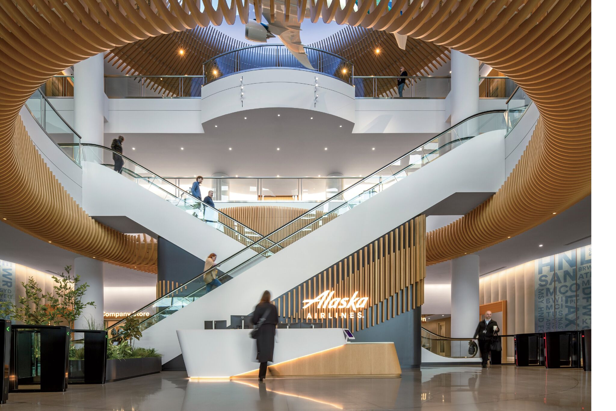 Modern lobby of Alaska Airlines headquarters with a central reception desk, large staircase, wood ceiling accents, and several people walking or using the stairs.