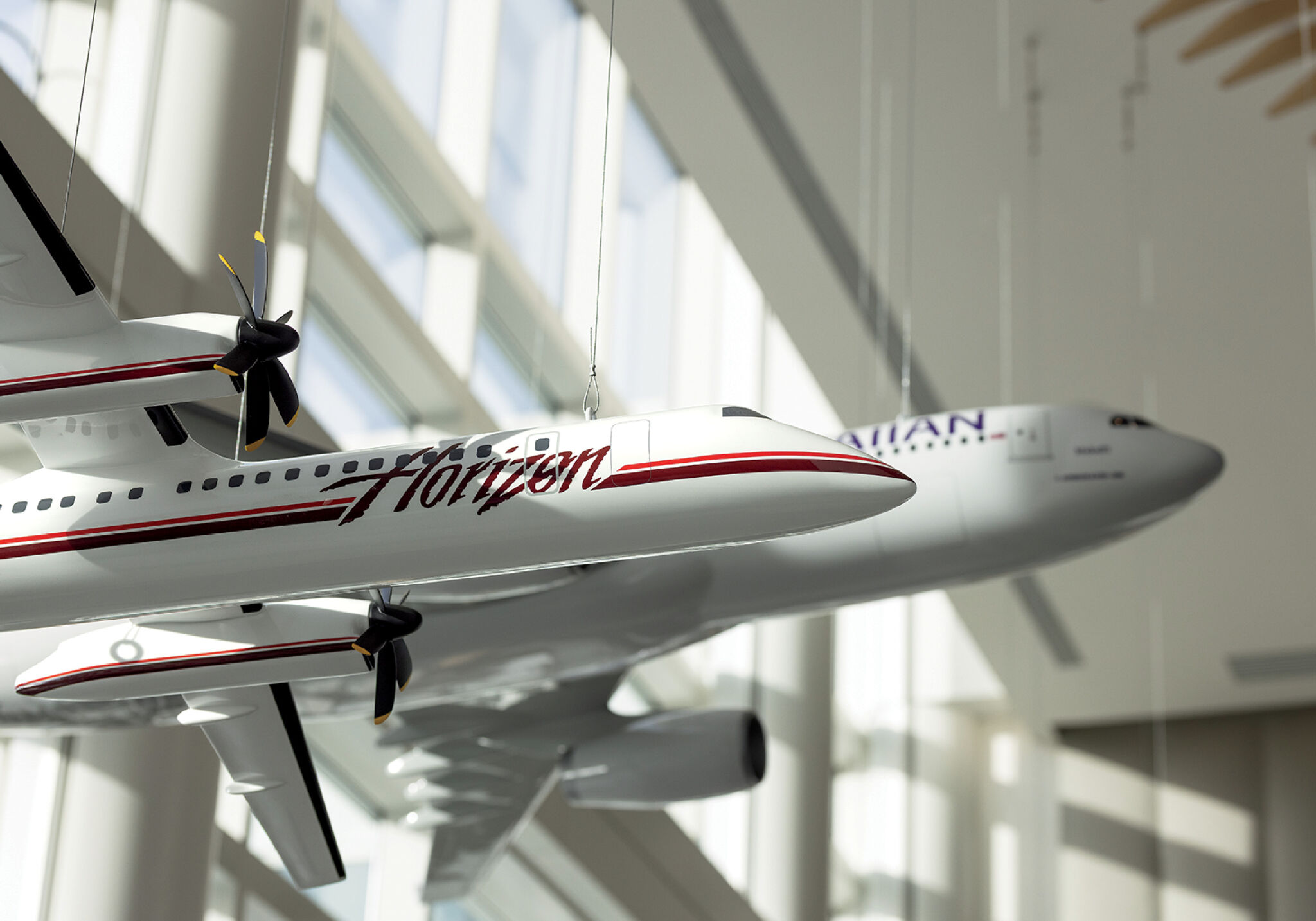 Two model airplanes hang from the ceiling in a bright, modern space with large windows and sunlight streaming in.