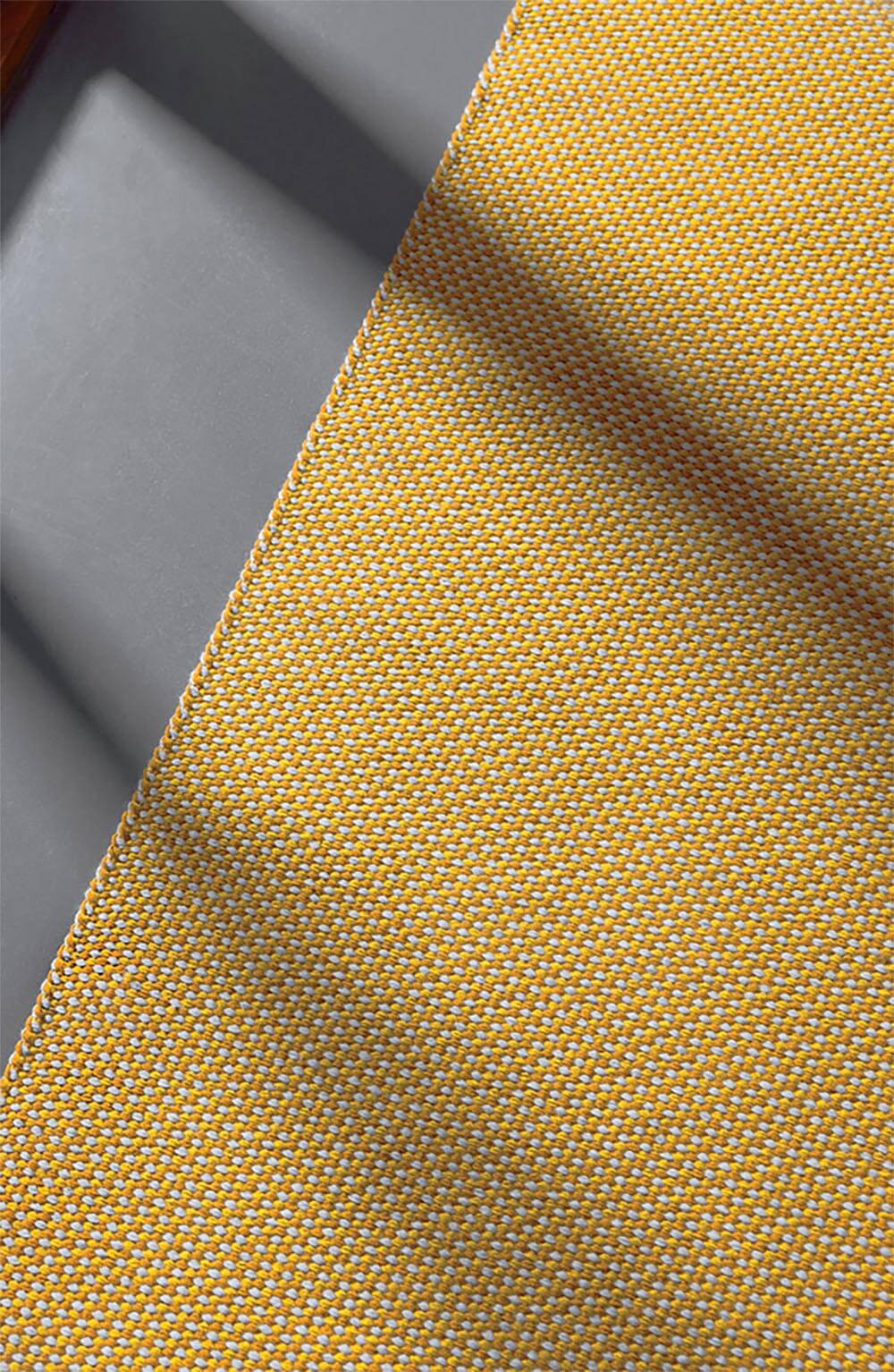 A close-up of yellow and white woven fabric next to a gray surface with diagonal shadows cast across both.