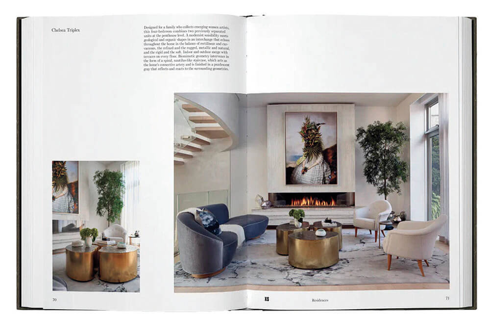 Open book showing a modern living room with neutral furniture, round gold tables, large artwork above a fireplace, and tall green plants. Marble floors and large windows are visible.