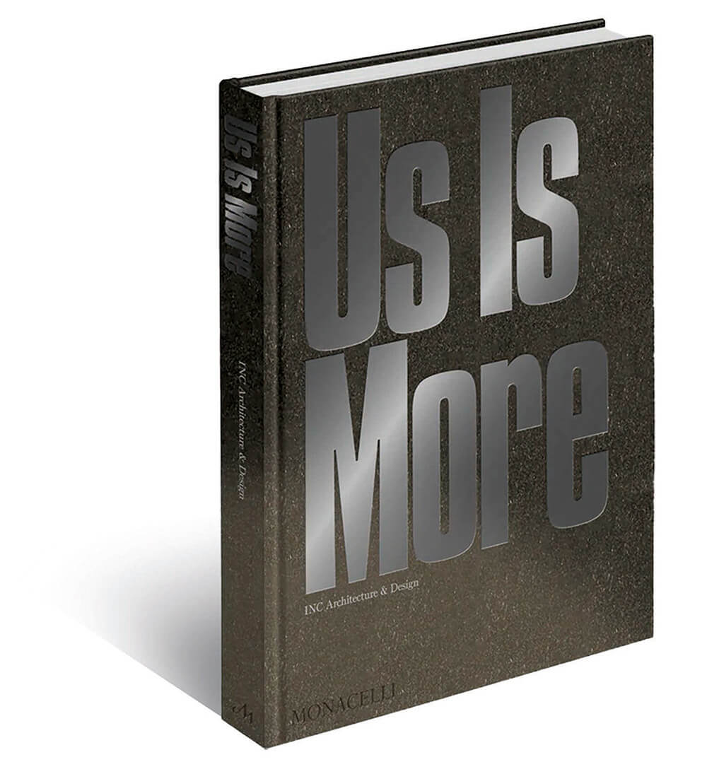 A hardcover book titled “Us Is More” by INC Architecture & Design, published by Monacelli, featuring large metallic silver text on a textured dark cover.