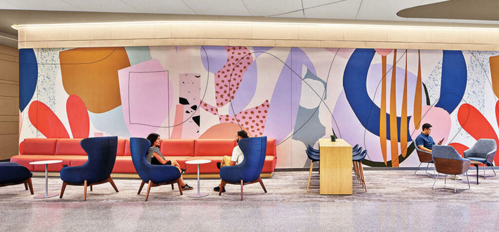 People sitting on lounge furniture in a lobby featuring a large, colorful abstract mural.