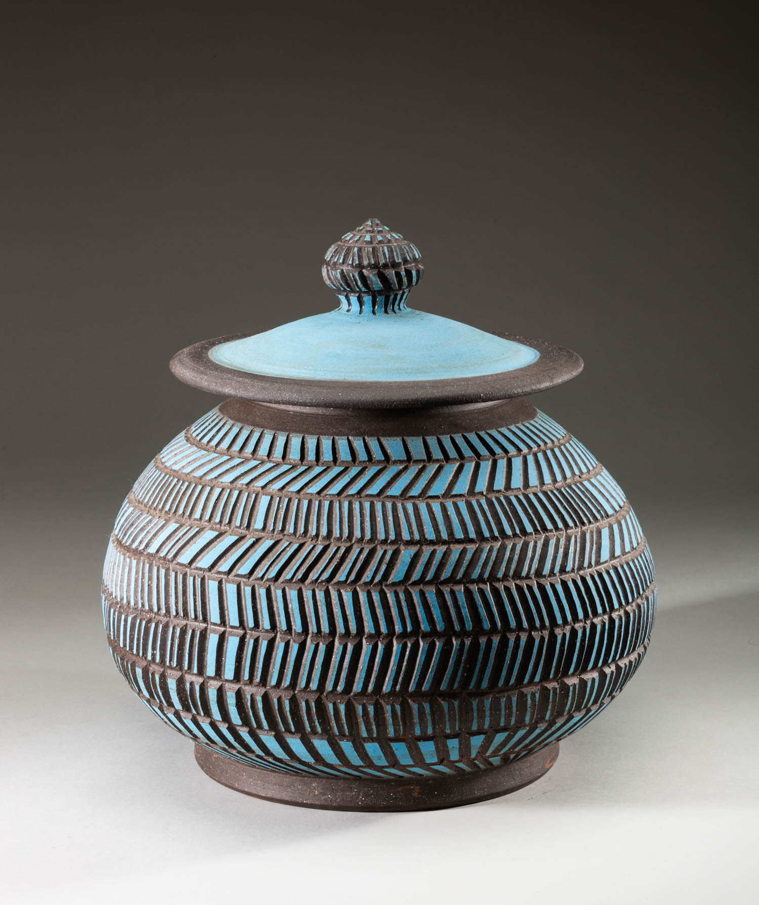 Round ceramic jar with lid, decorated with alternating horizontal bands of blue glaze and textured dark lines. The lid has a matching pattern and a knob handle on top.