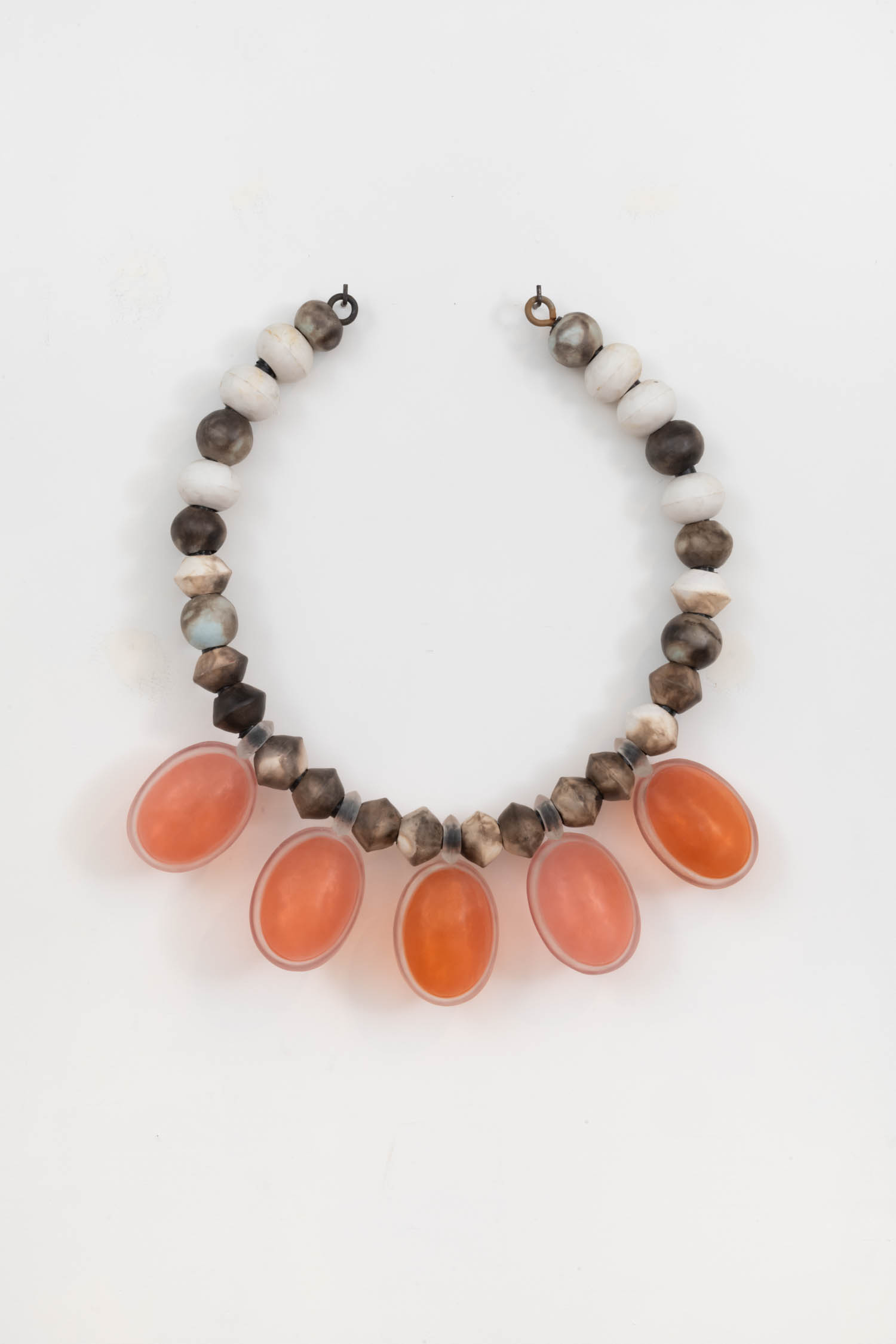 A beaded necklace with alternating white and brown beads, featuring five large oval orange stones hanging at the center.