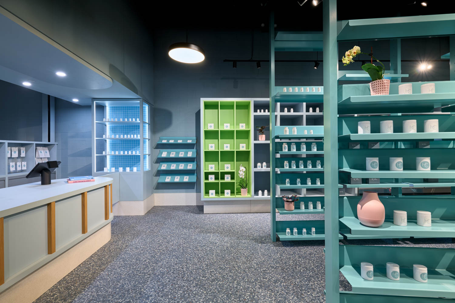 Modern retail store interior with teal and green shelving, a counter on the left, and various white products and decorative items neatly arranged throughout the brightly lit space.