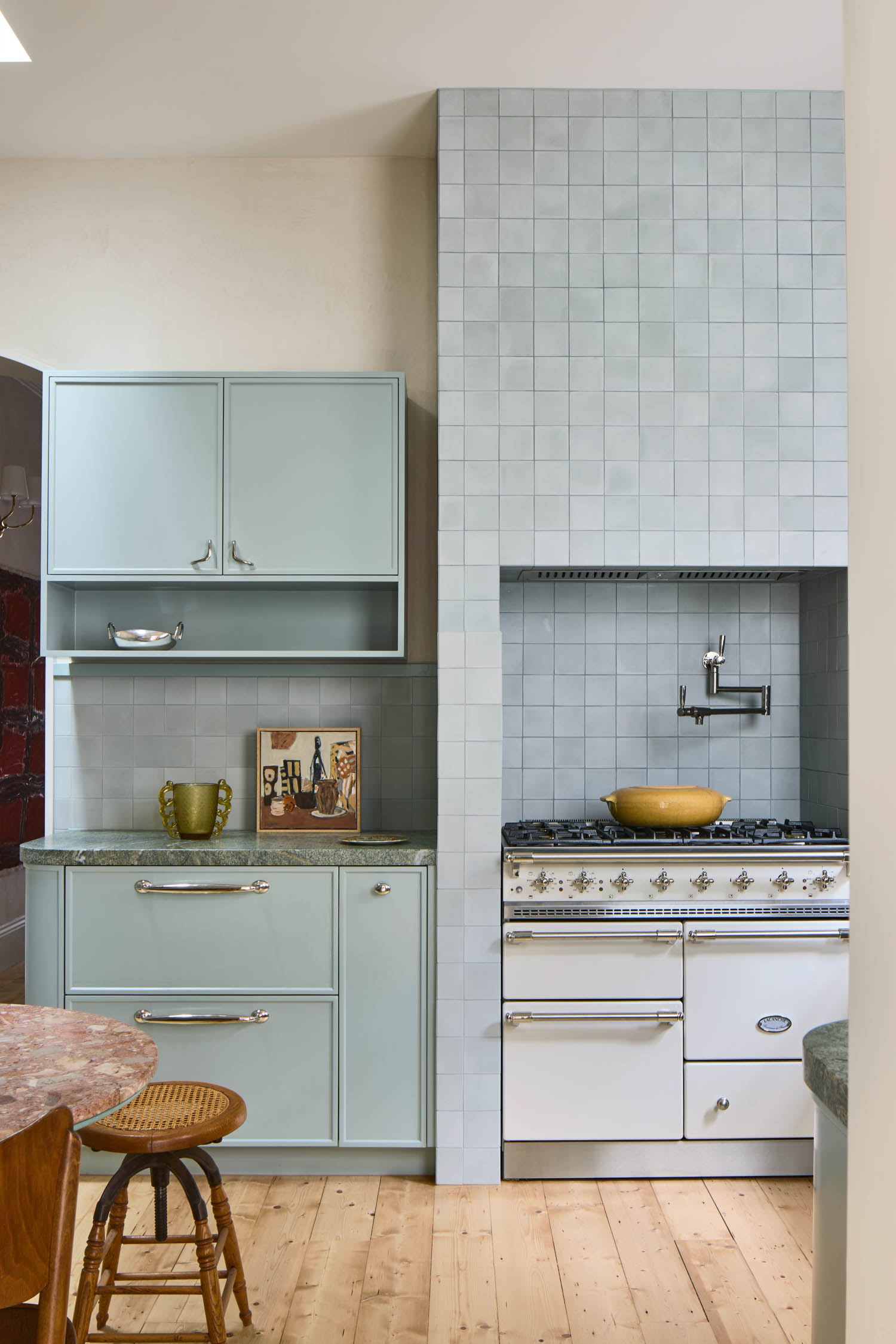 A pastel blue kitchen with tiled backsplash, a vintage-style stove, green countertop, wooden stool, and decorative items on the counter.