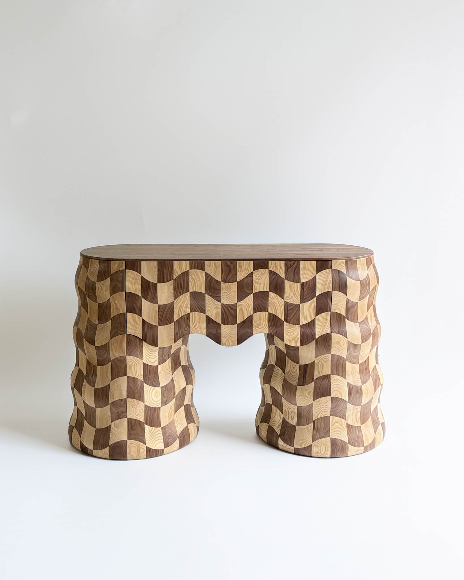 A wooden table with a wavy, checkered pattern in light and dark wood tones, featuring two curved legs and a rectangular top.