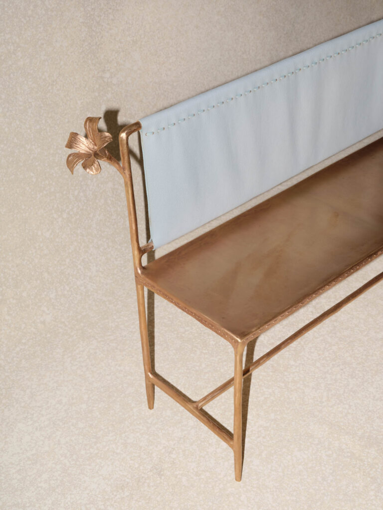 Metal bench with a light blue fabric backrest and a decorative flower on the left end, set against a neutral background.